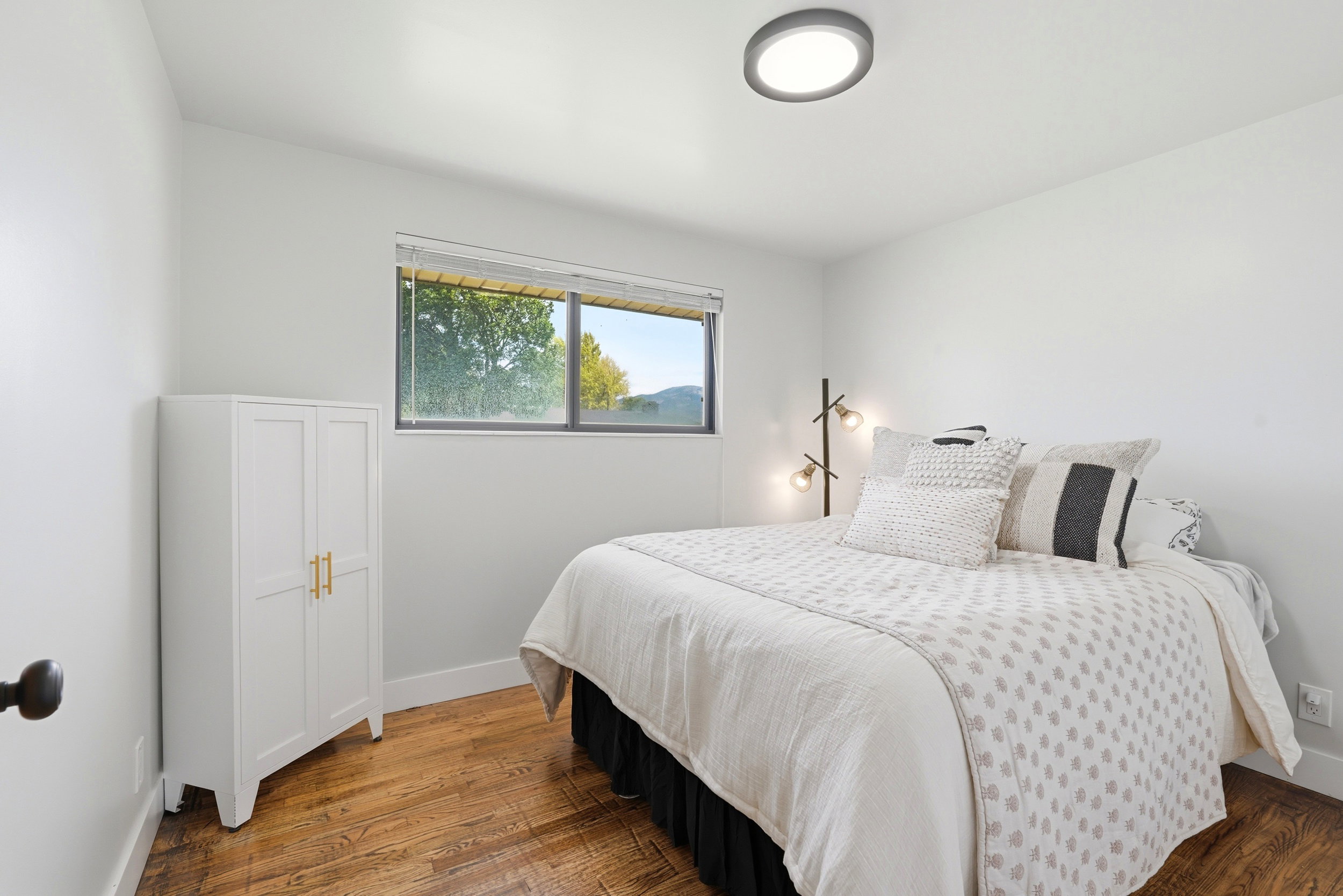 Bedroom featuring wood-finish flooring, a contemporary flush-mount ceiling light, white baseboards, and a window with a mountain backdrop
