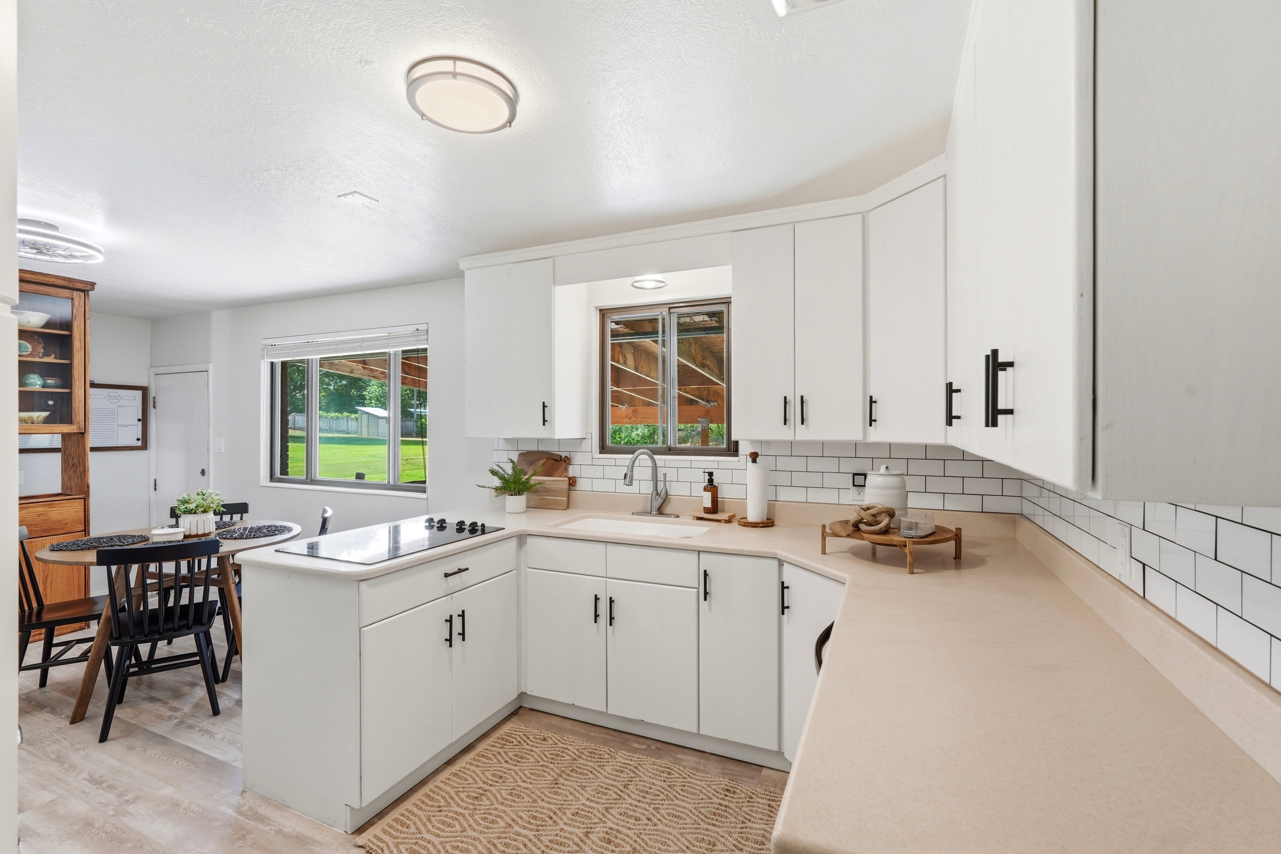 Bright kitchen featuring white cabinetry with black hardware, a subway tile backsplash, and a built-in cooktop