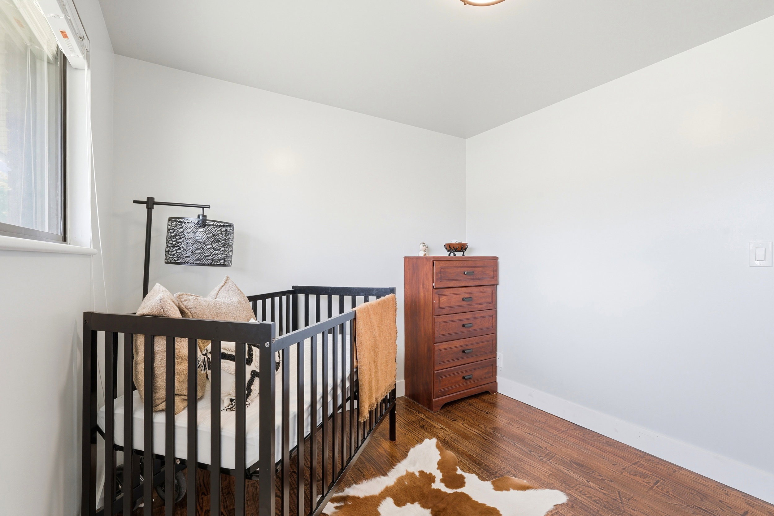 Bright room featuring a window with blinds, light-toned walls, and wood-finish flooring