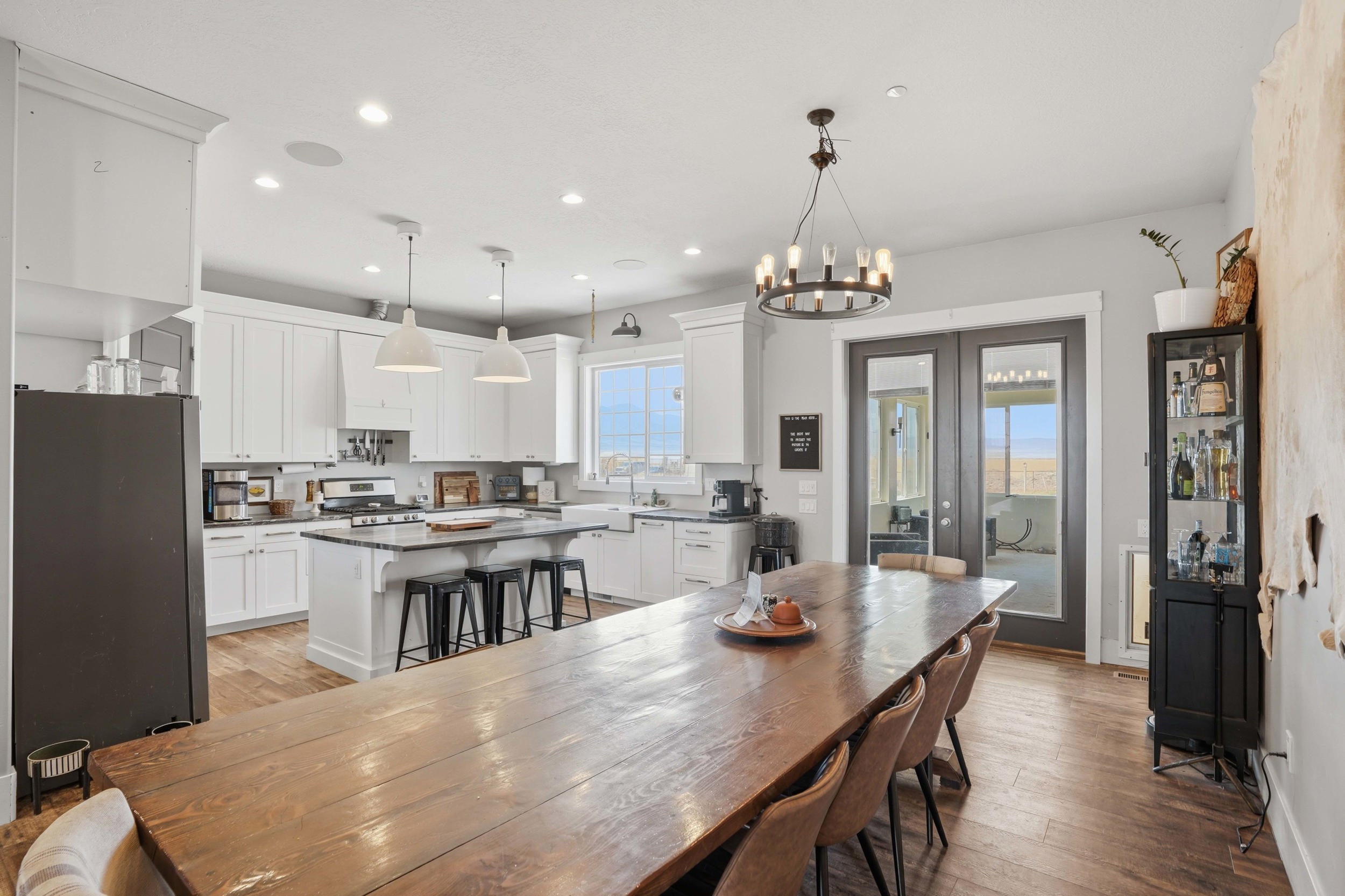 Open-concept dining and kitchen space featuring wood-finish flooring, white cabinetry, a kitchen island with seating, a gas range, and double glass-paneled doors