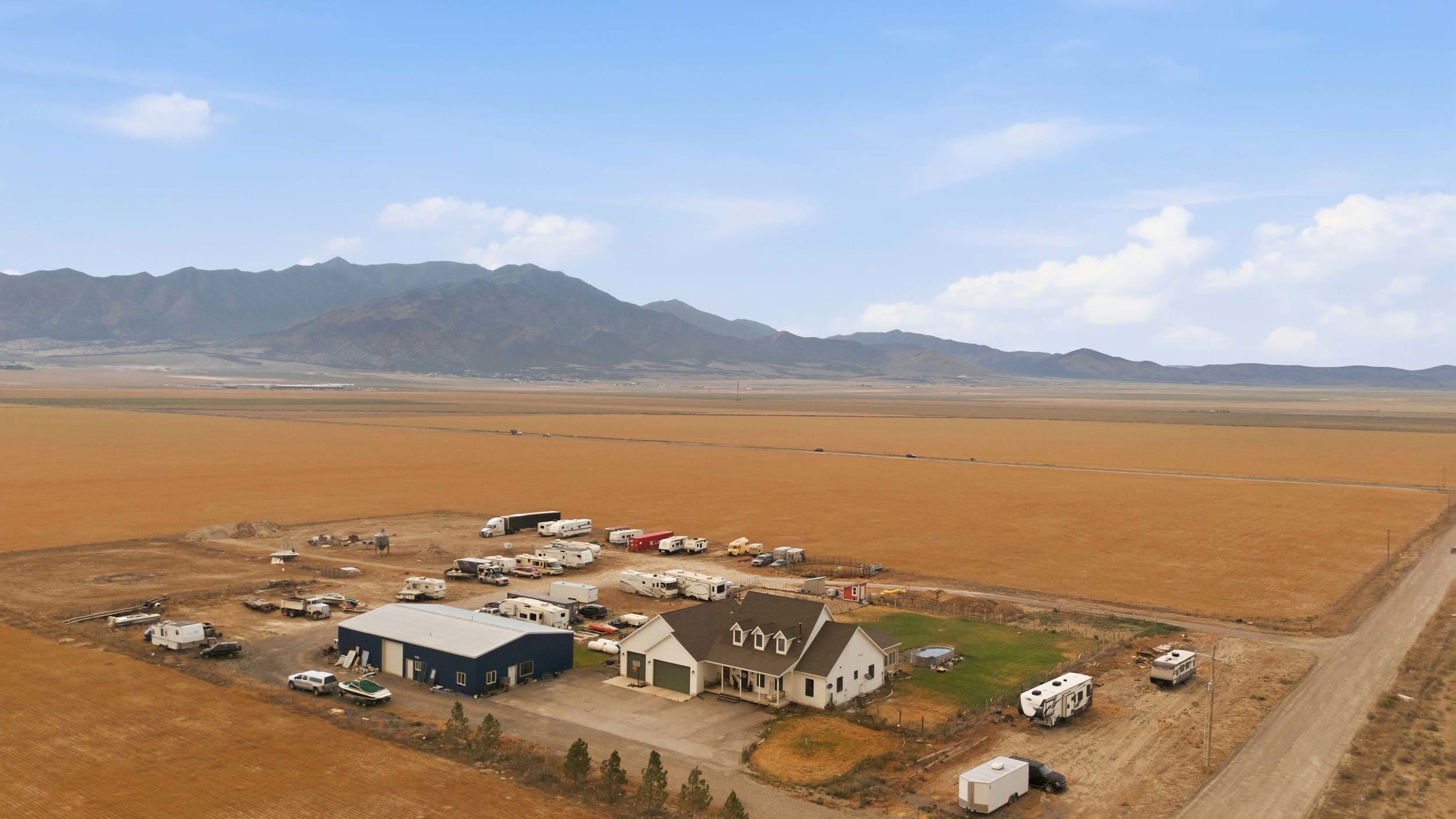 Rural property featuring a single-family residence, a large blue outbuilding, a smaller white outbuilding, and expansive surrounding land