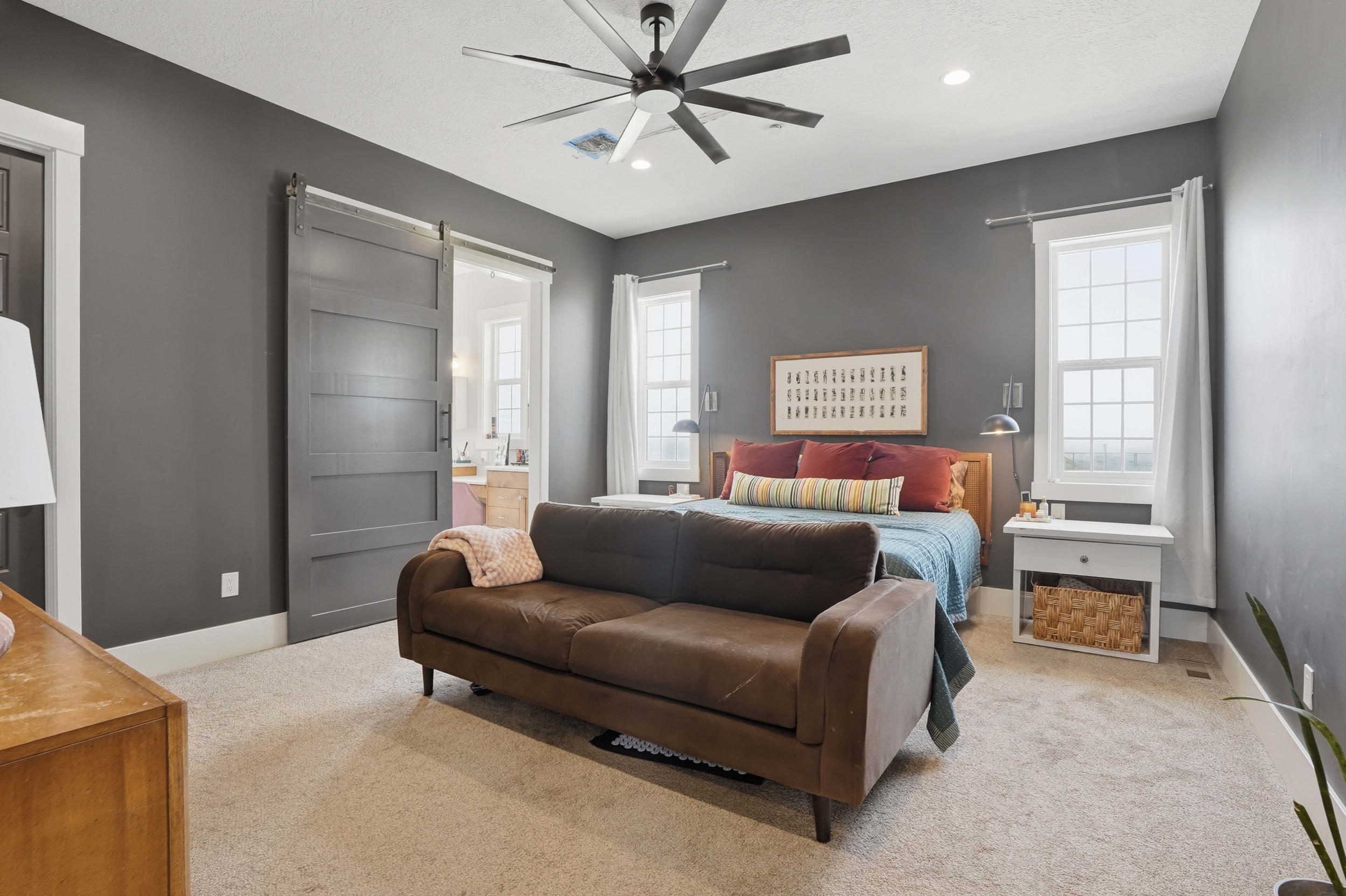 Spacious room featuring a dark gray barn door, two large windows with white trim, a ceiling fan, and recessed lighting