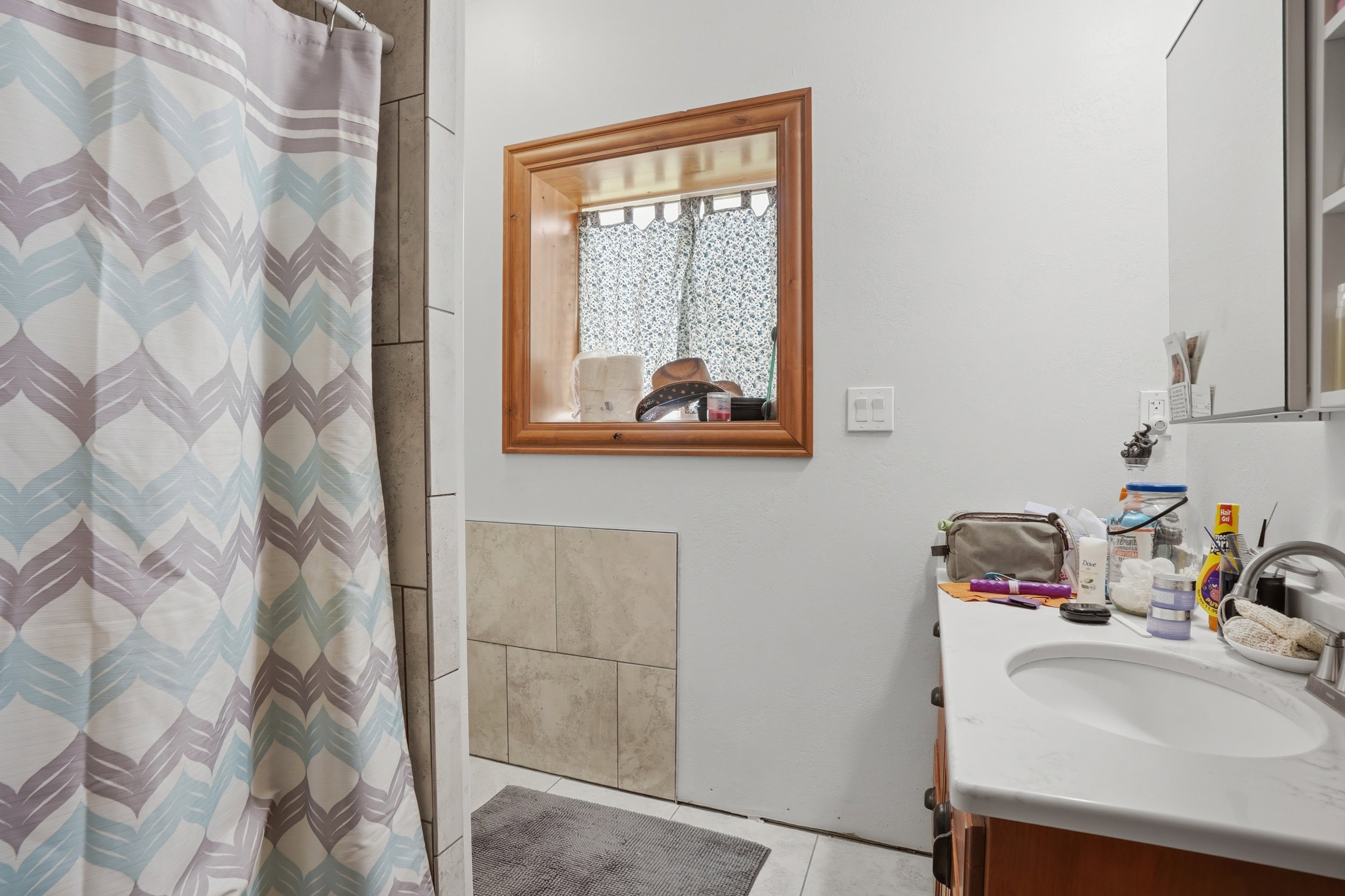 Bathroom featuring a wood-finish vanity with a white countertop and integrated sink, a framed mirror, and light-toned wall tiling