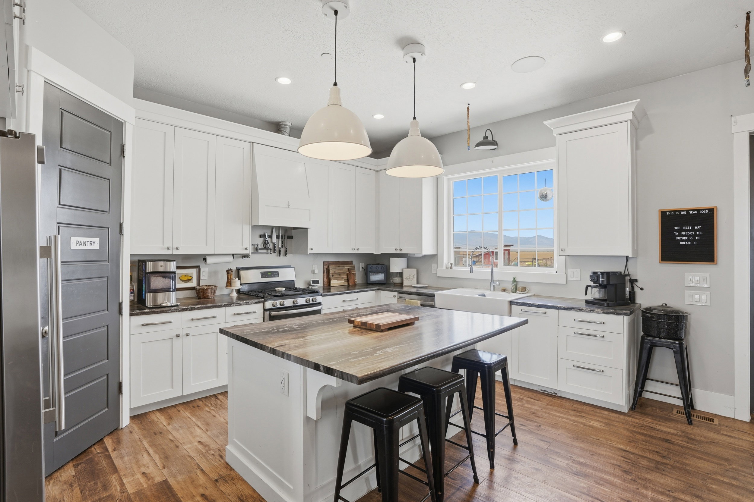 Kitchen featuring wood-finish flooring, white cabinetry, a central island with countertop seating, and a large window above a farmhouse-style sink