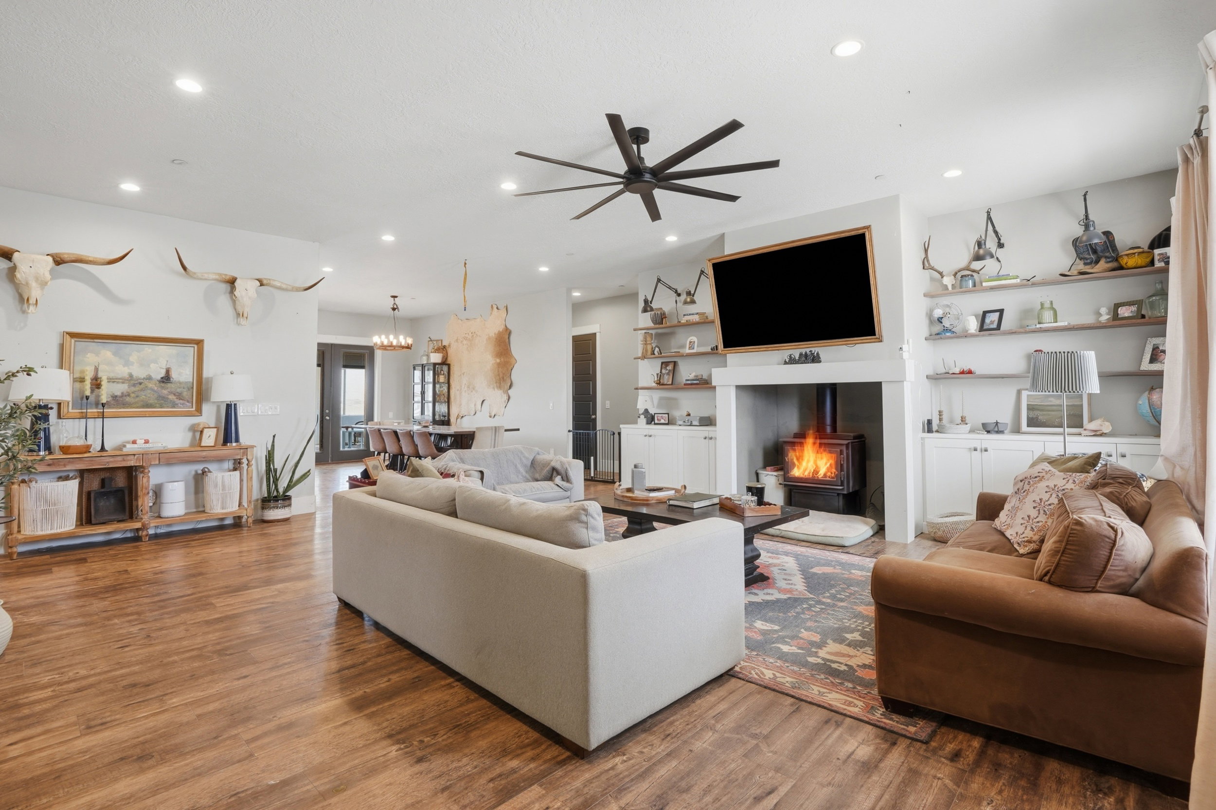 Spacious living area featuring wood-finish flooring, a built-in wood-burning stove, white mantel, recessed lighting, and a modern ceiling fan