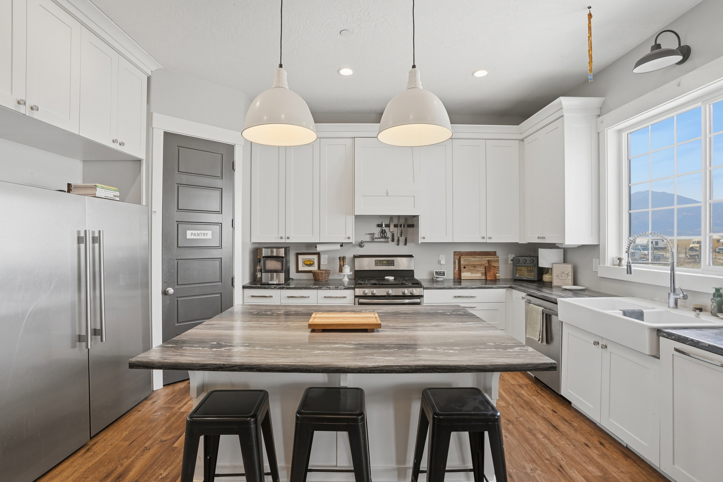 Spacious kitchen featuring an expansive center island, white shaker cabinetry, stainless steel appliances, a farmhouse sink, and wood-finish flooring