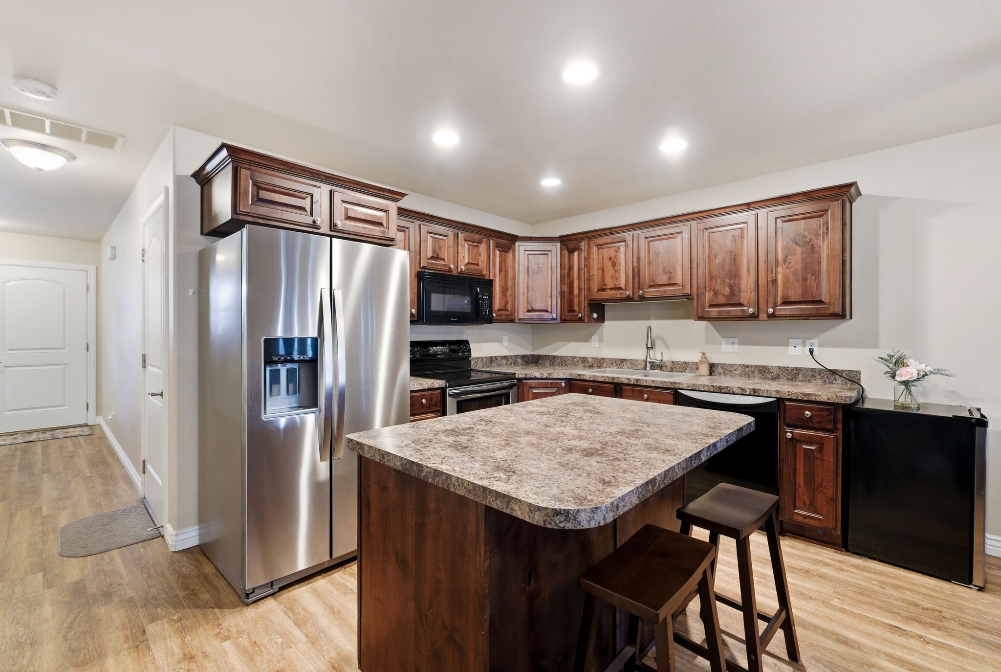 Kitchen with black appliances, a kitchen island, a kitchen breakfast bar, light wood-style flooring, and recessed lighting