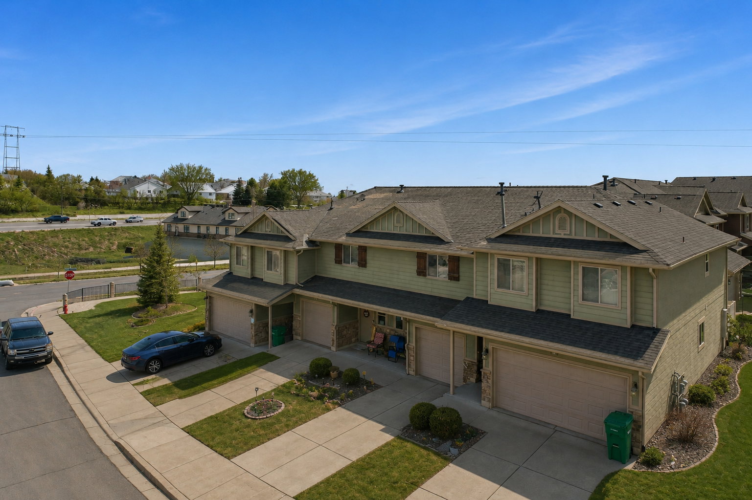 Multi-level townhome exterior featuring light green siding, dark shingle roofing, and attached garages