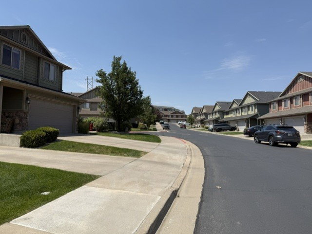 Residential street featuring a row of two-story homes with attached garages, light green siding, and peaked roofs