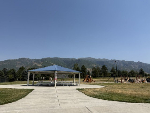 Expansive park area featuring a blue-roofed gazebo, concrete pathways, and green space