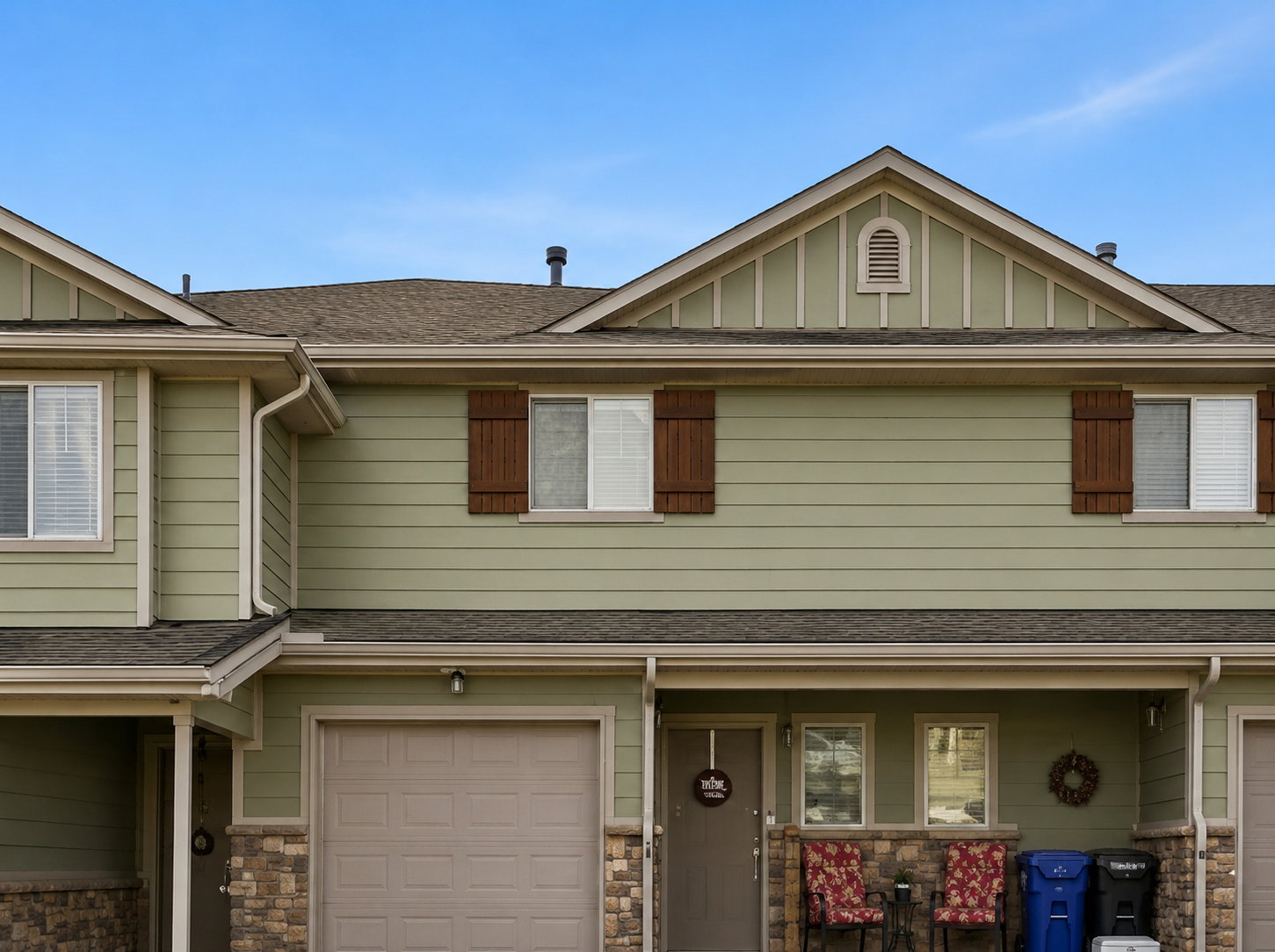 Multi-level exterior featuring light green siding, decorative brown window shutters, and a prominent gable with a louvered vent