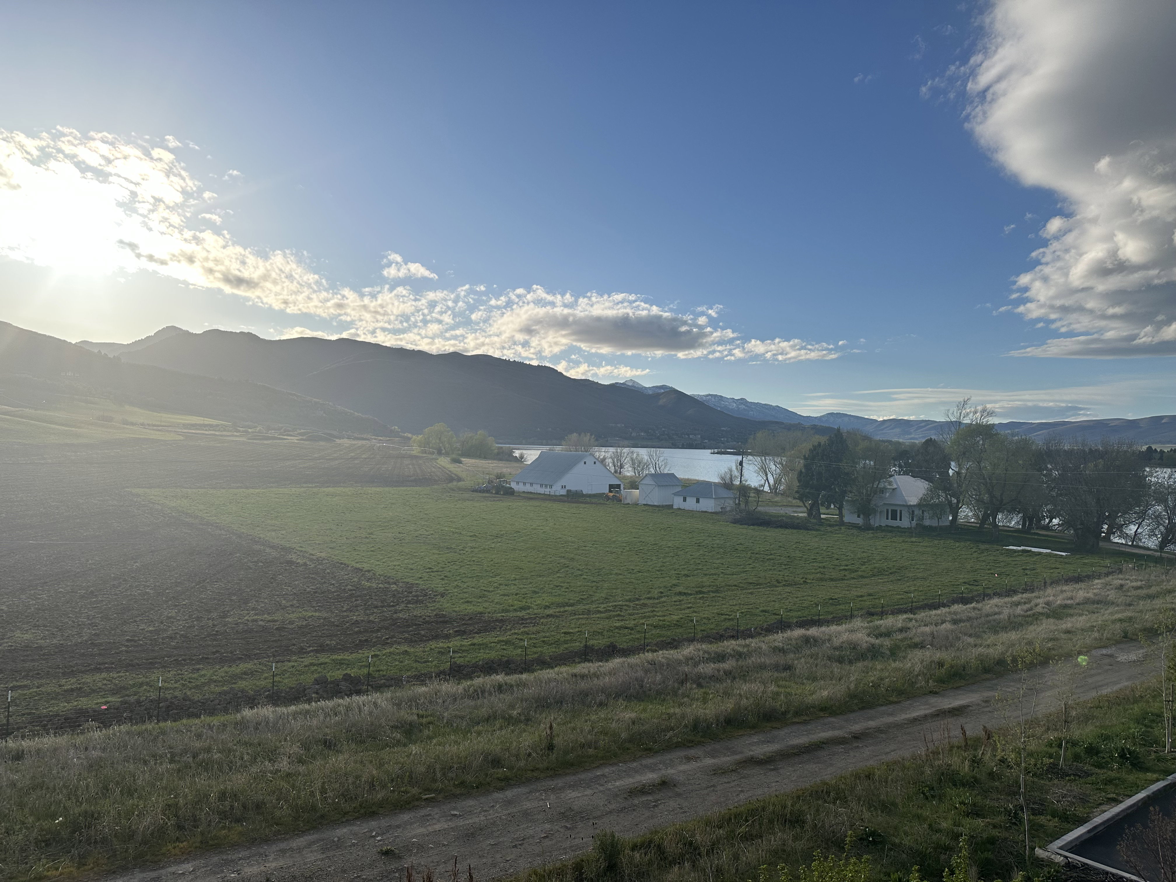 Expansive landscape featuring agricultural fields, a distant body of water, and surrounding mountains