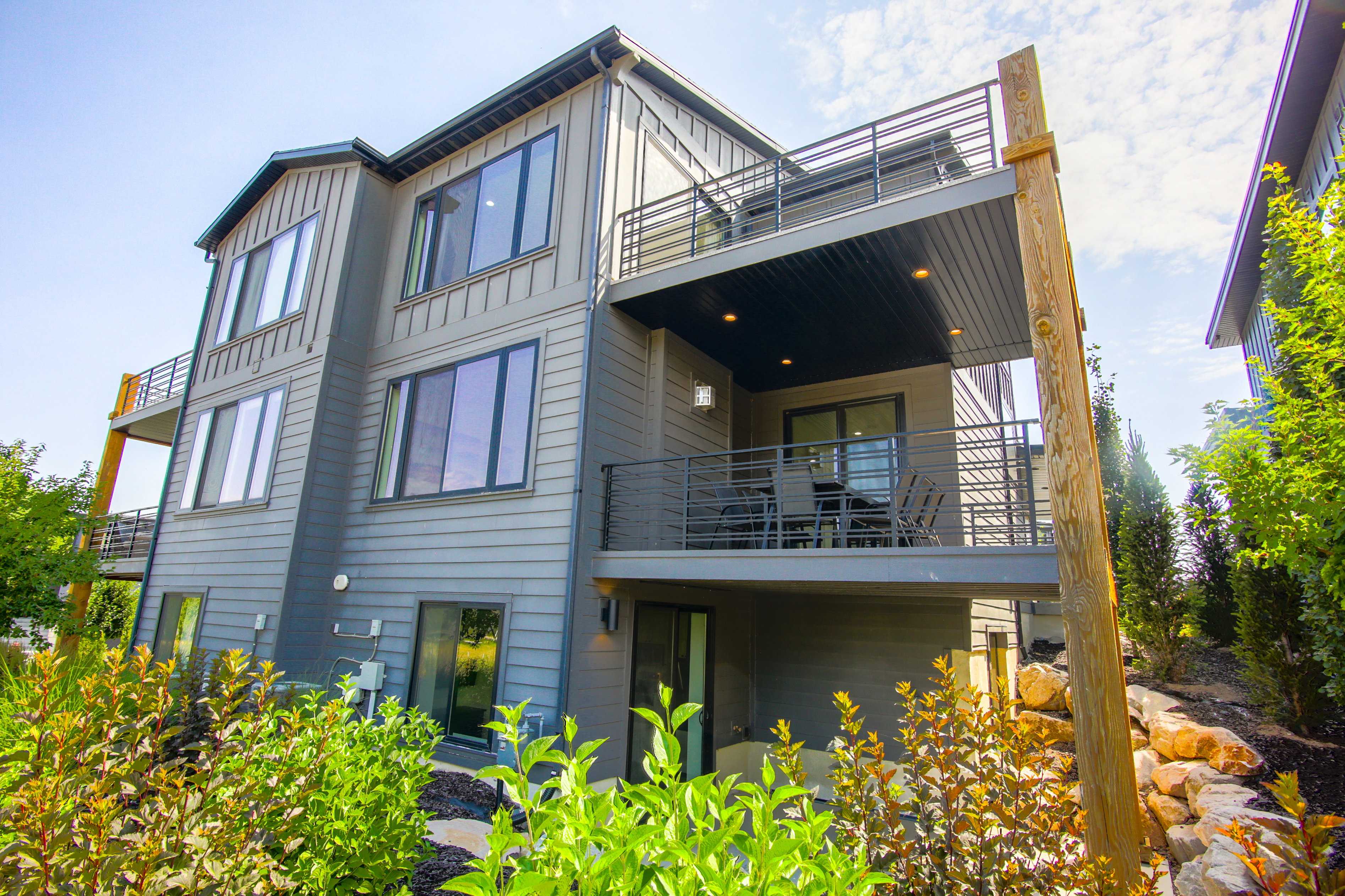 Contemporary multi-level exterior with board and batten siding, multiple balconies featuring metal railings, and a covered patio with recessed lighting