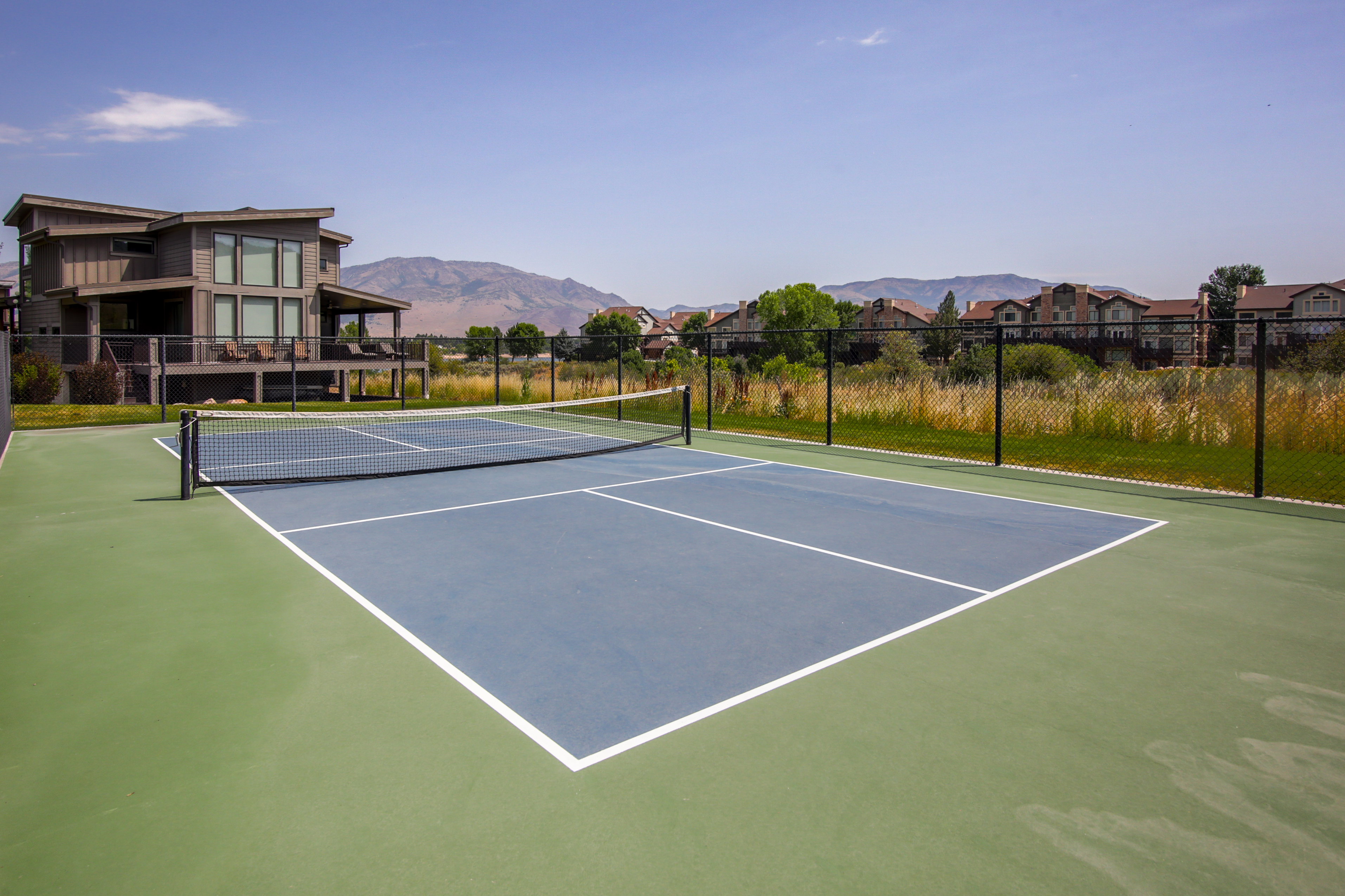 Outdoor tennis court featuring a blue playing surface with white lines and green surrounding court