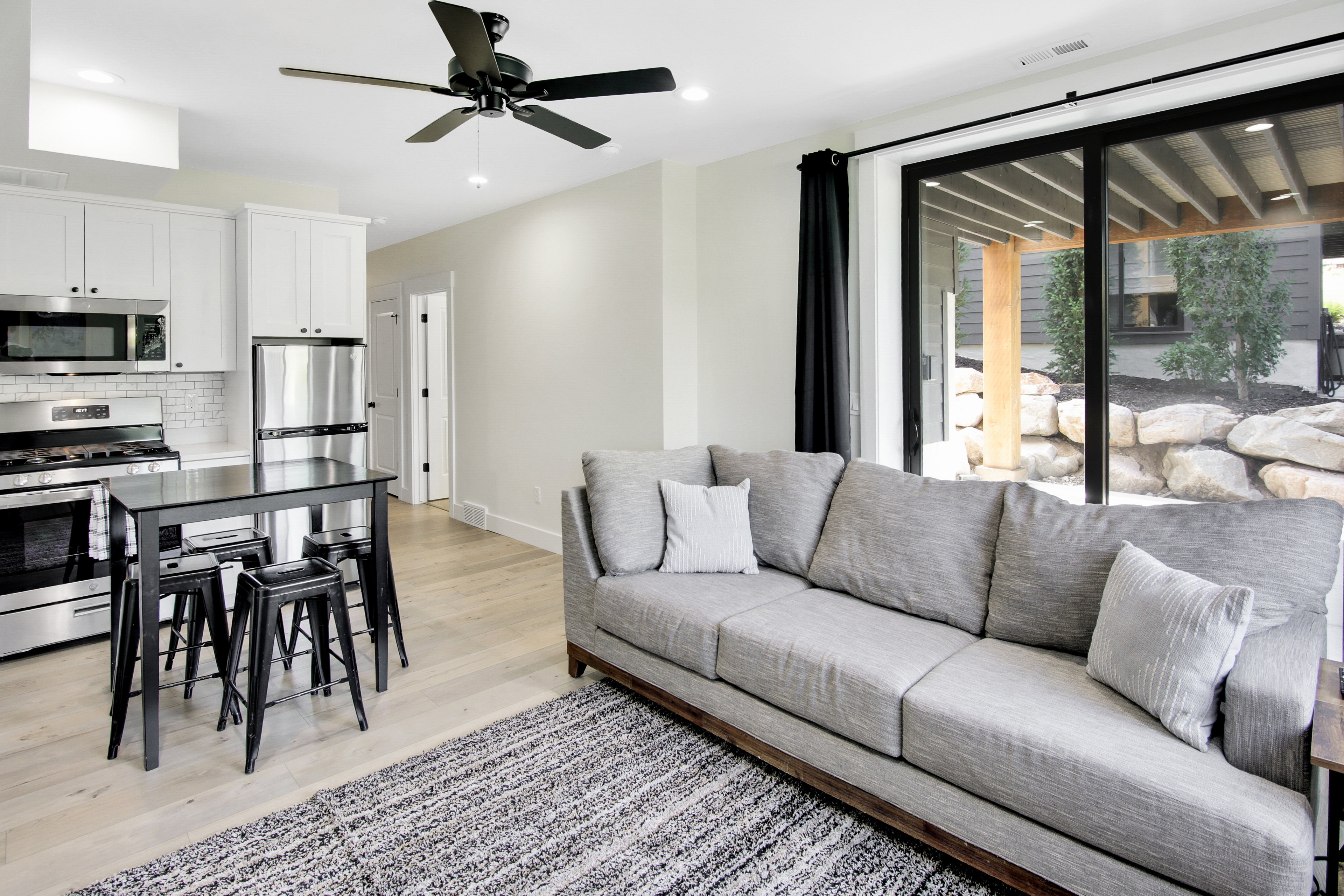 Open-concept living area featuring light wood-finish flooring, a modern black ceiling fan, and sliding glass doors