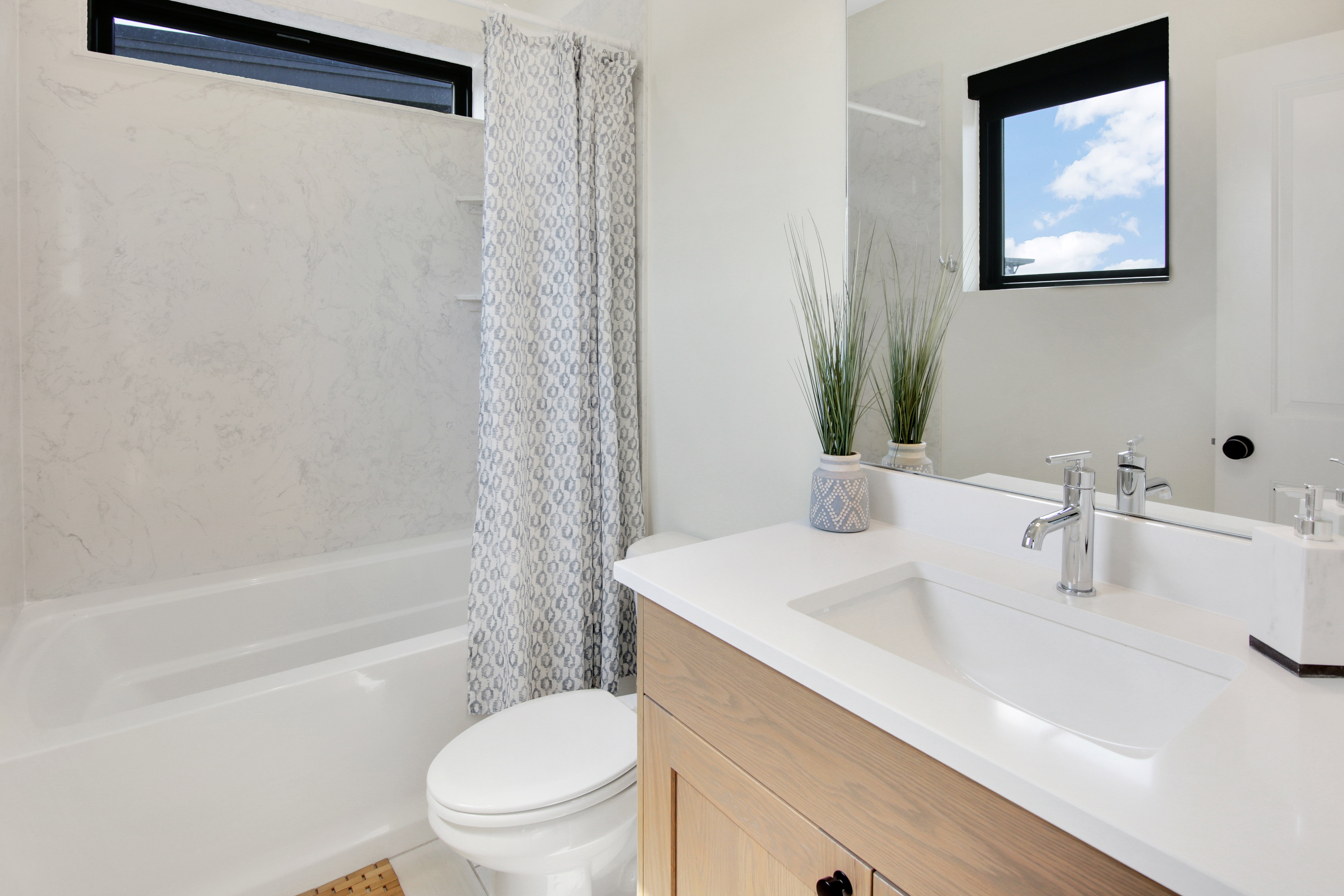 Bathroom featuring a white tub with light-toned tiled surround, a long, narrow transom window, and a single vanity with a light wood-finish base and a white countertop