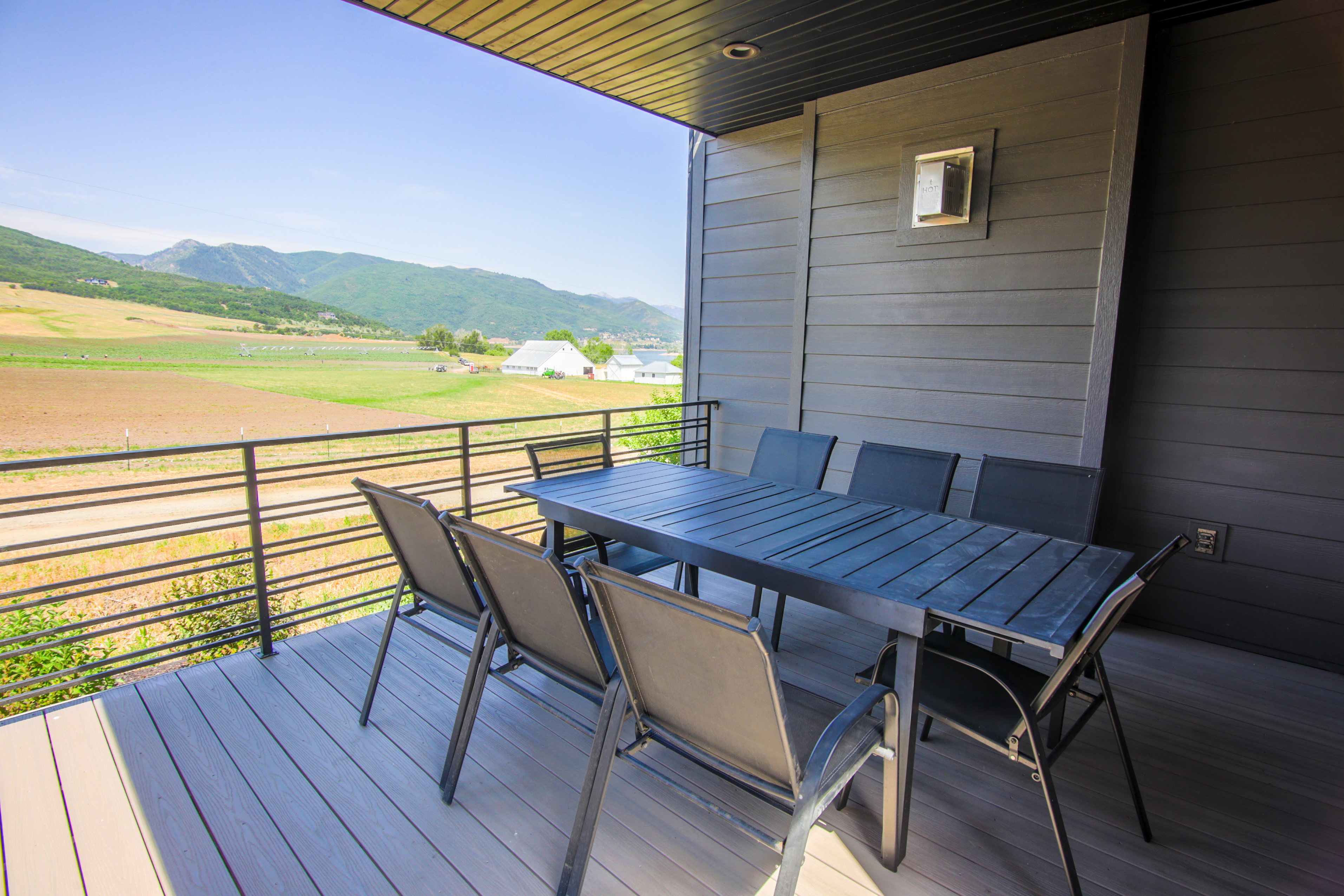 Covered outdoor patio featuring composite decking, horizontal metal railing, and an expansive mountain and field backdrop