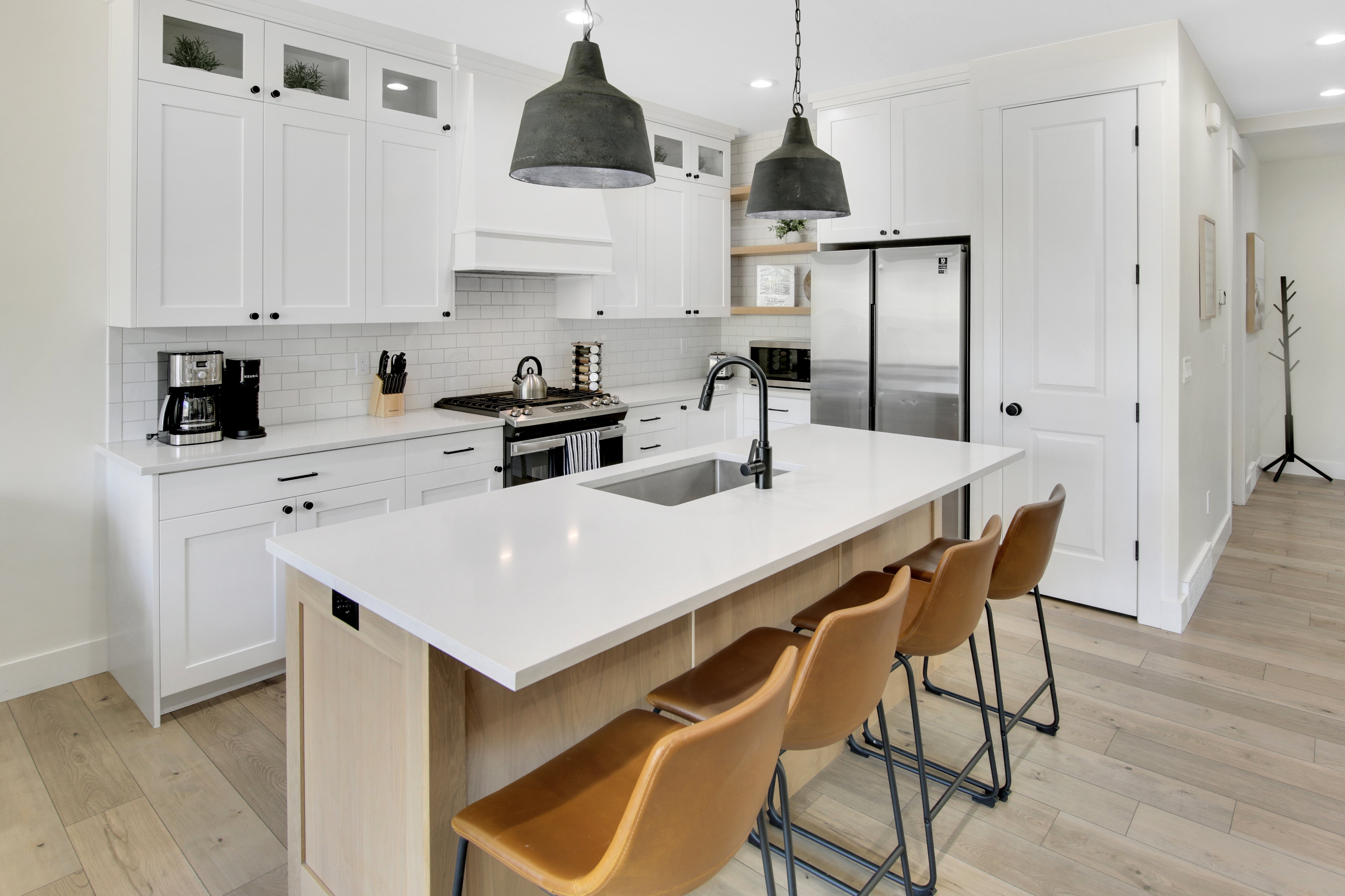 Modern kitchen featuring white shaker cabinetry, stainless steel appliances, a center island with sink and seating, wood-finish flooring, and subway tile backsplash