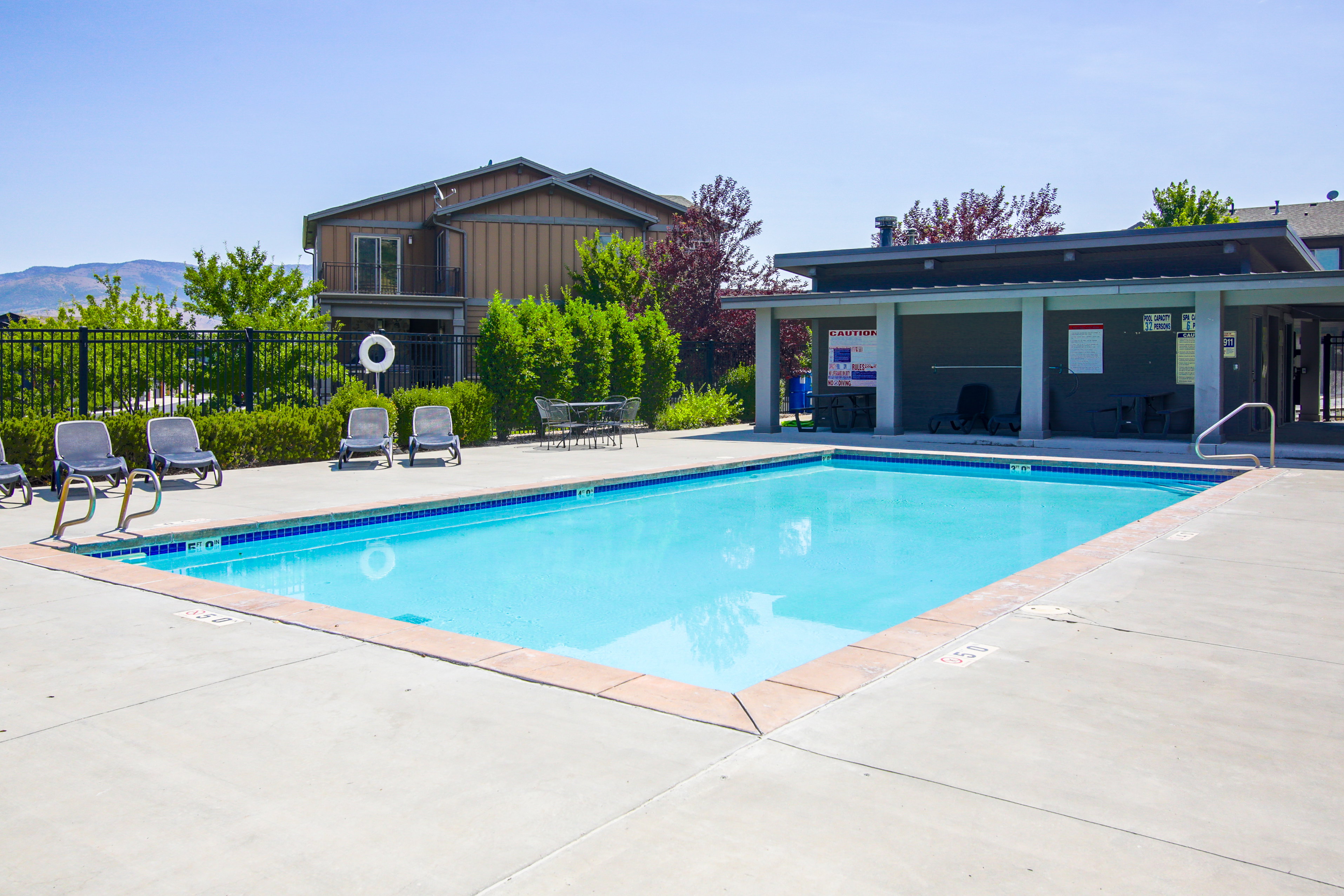 Outdoor swimming pool with concrete decking, a surrounding metal fence, and a covered patio area