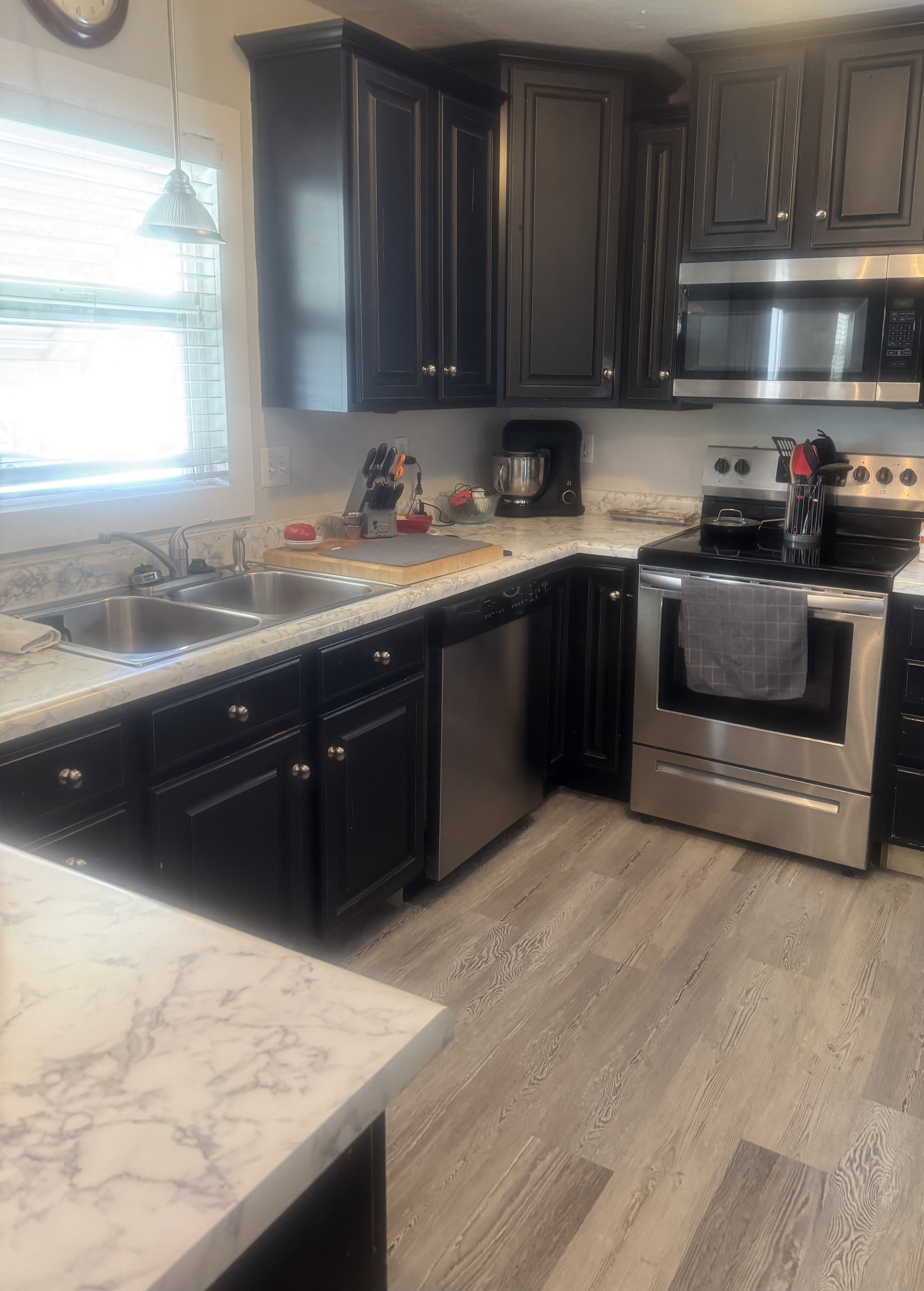 Kitchen featuring dark cabinetry, stainless steel appliances, marble-look countertops, and wood-finish flooring