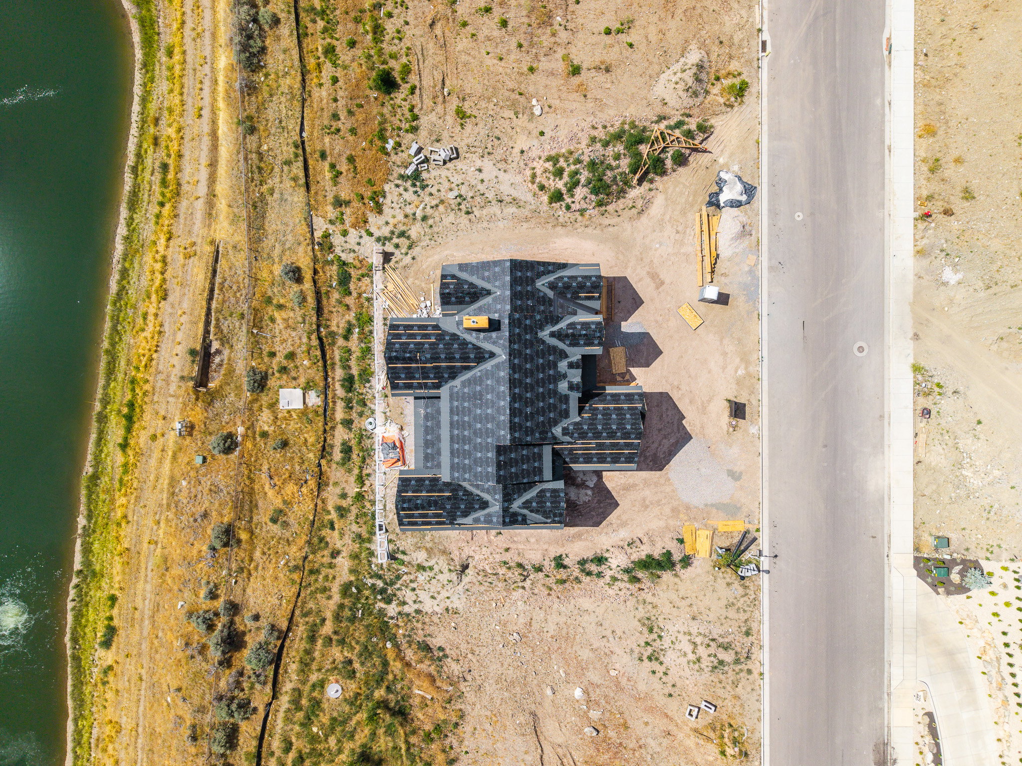 New construction home featuring a complex roofline with dark shingles, a paved street, and a waterfront property line