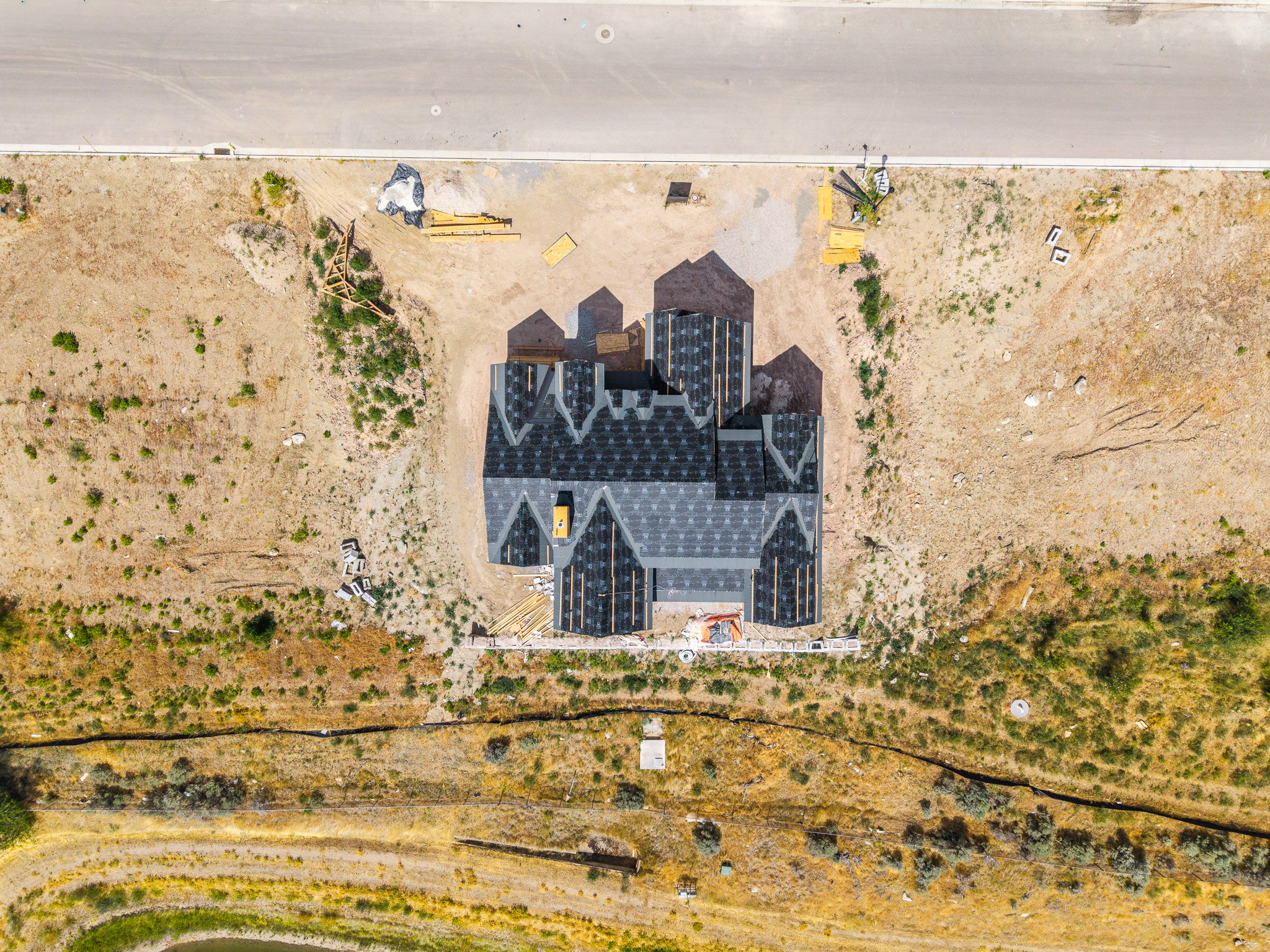 New construction residential structure featuring a multi-gabled roof with dark shingle application, located on a lot with undeveloped land