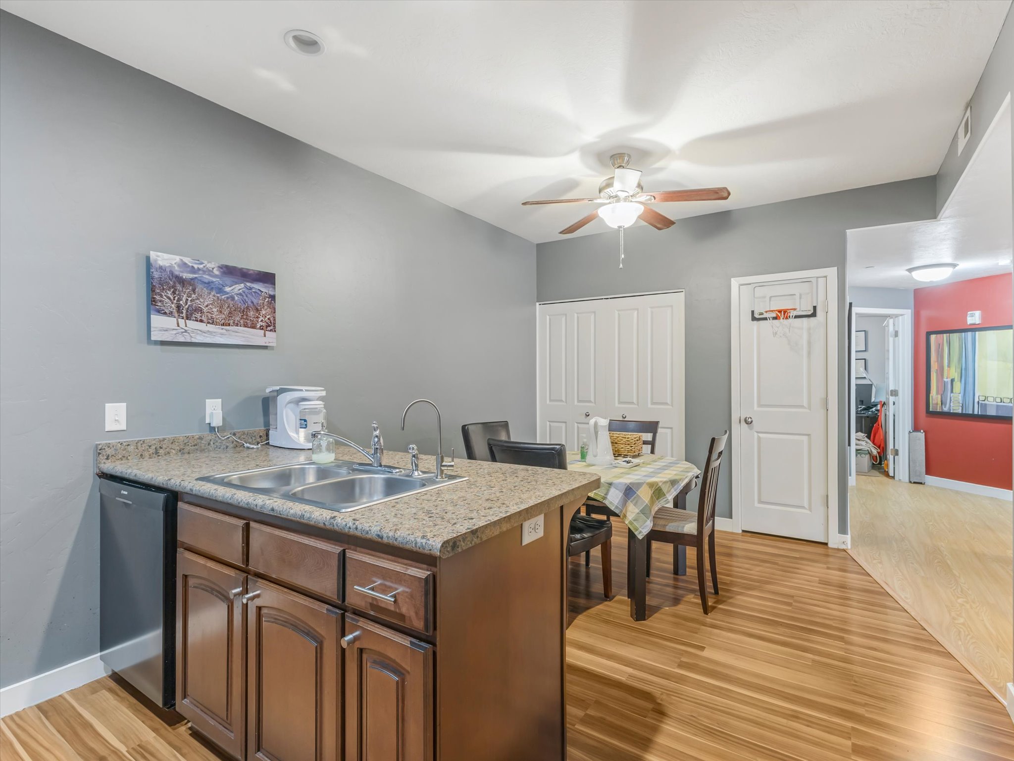 Kitchen featuring wood-finish flooring, a double basin stainless steel sink, brown cabinetry with brushed nickel hardware, and granite-look countertops