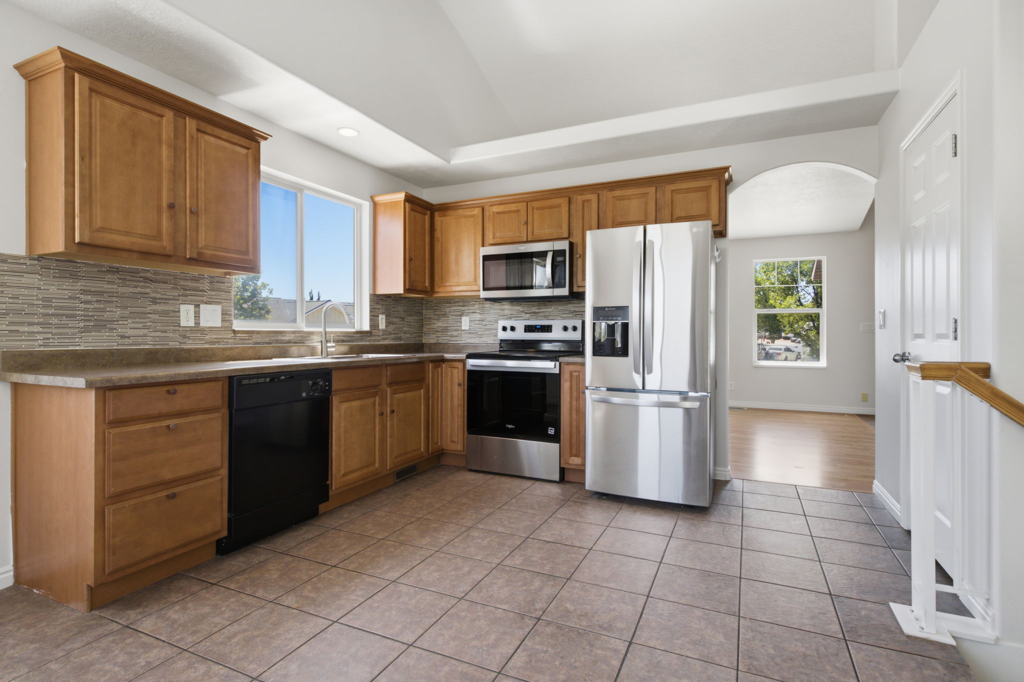 Kitchen featuring wood cabinetry, stainless steel appliances, mosaic tile backsplash, and a large window above the sink
