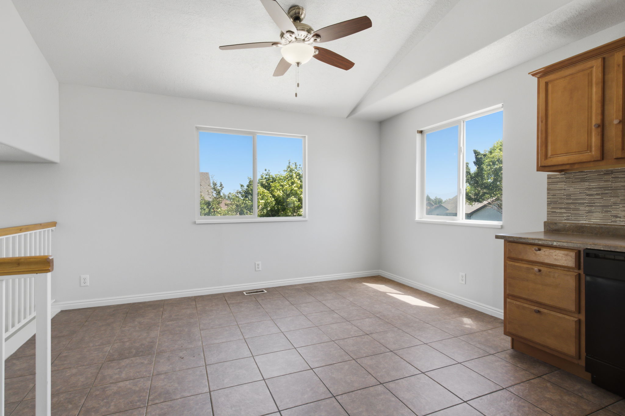 Spacious room featuring vaulted ceilings, a ceiling fan with integrated lighting, two large windows, tile flooring, and a built-in cabinetry and countertop area