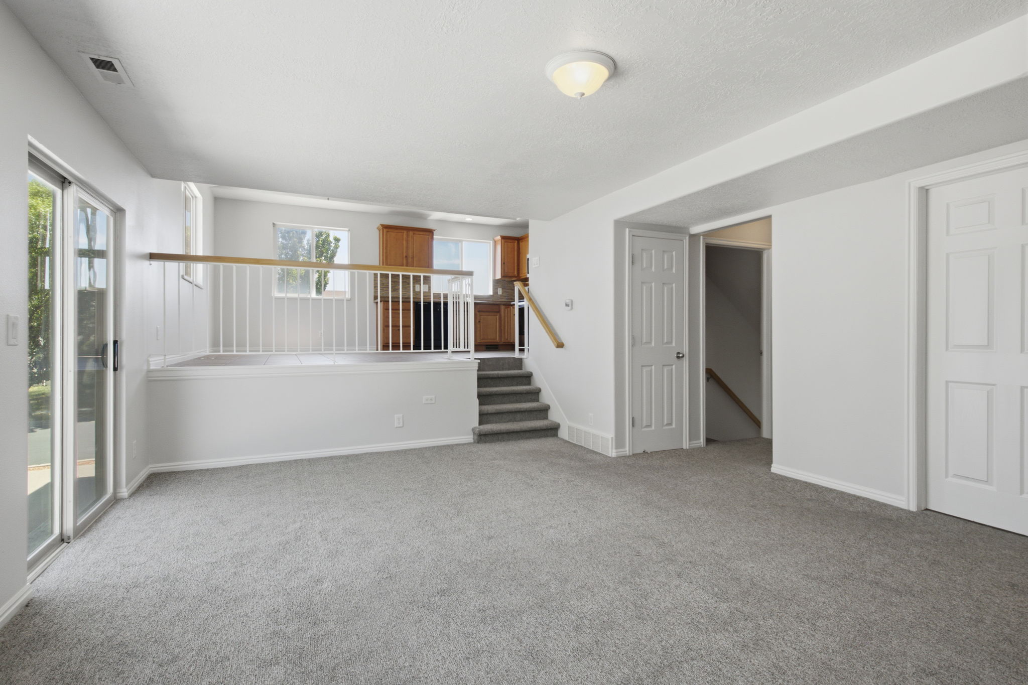 Open-concept living area featuring light gray carpet, white walls, and a sliding glass door