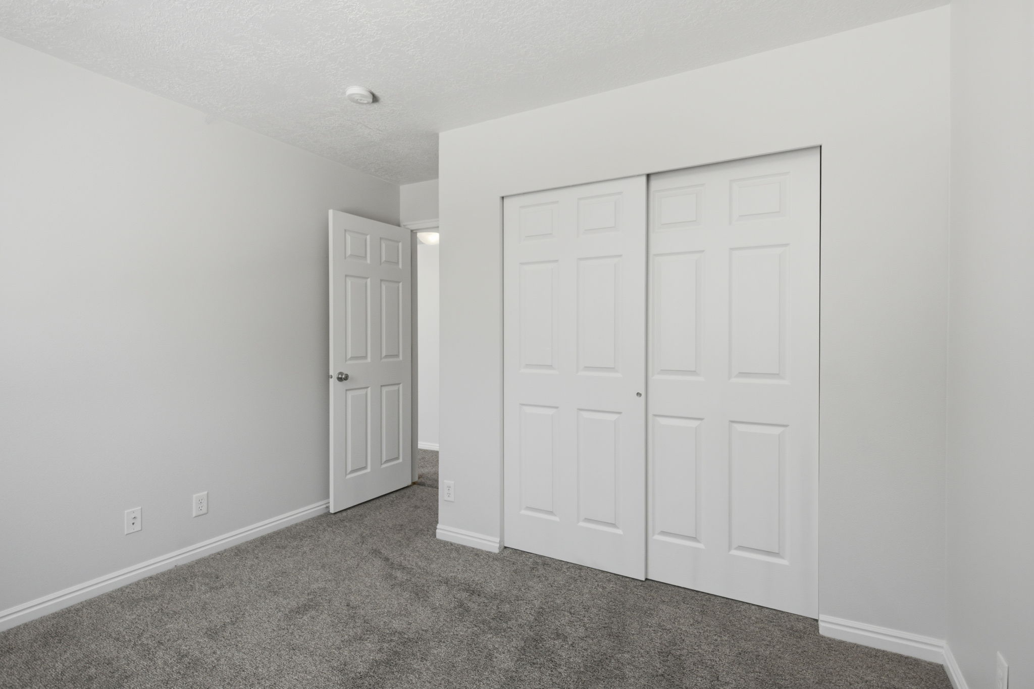 Carpeted room featuring a white six-panel interior door, white baseboards, and a bi-fold closet door