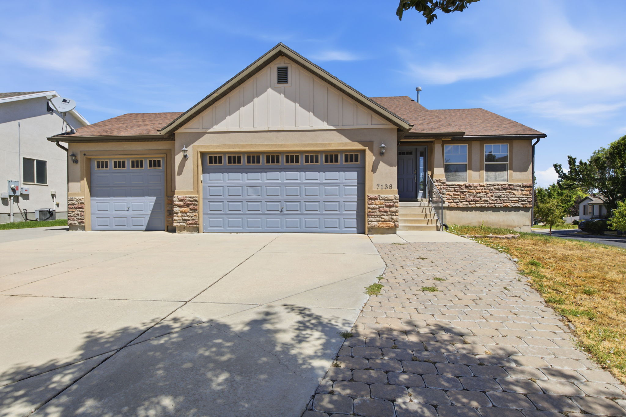 Ranch-style exterior featuring a gable roof, two-car garage, stone veneer accents, and a paved walkway