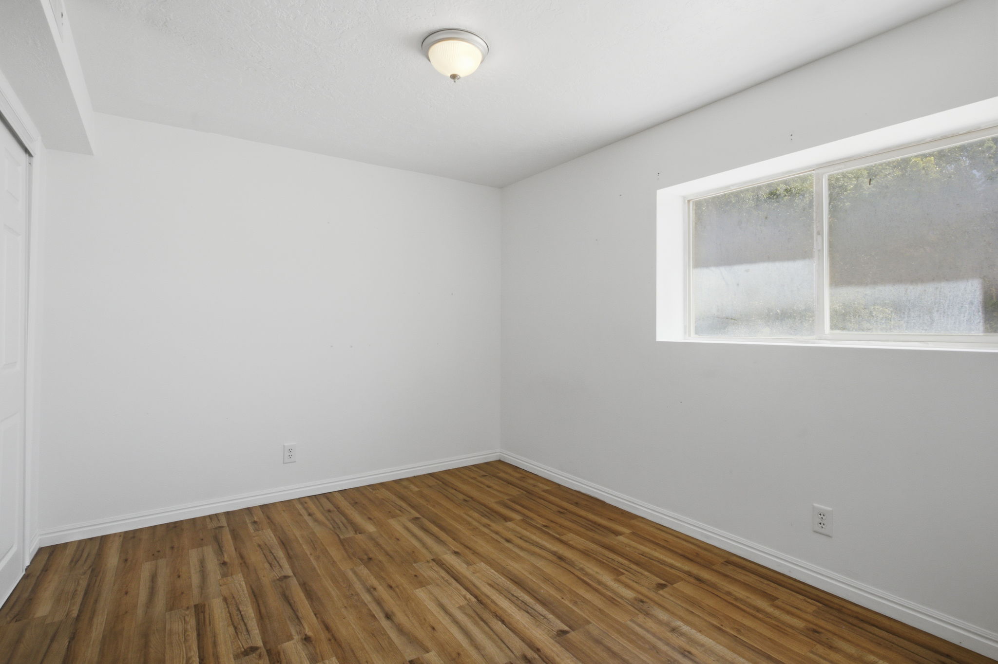 Room featuring wood-finish flooring, white baseboards, a single window, and a flush mount ceiling light fixture
