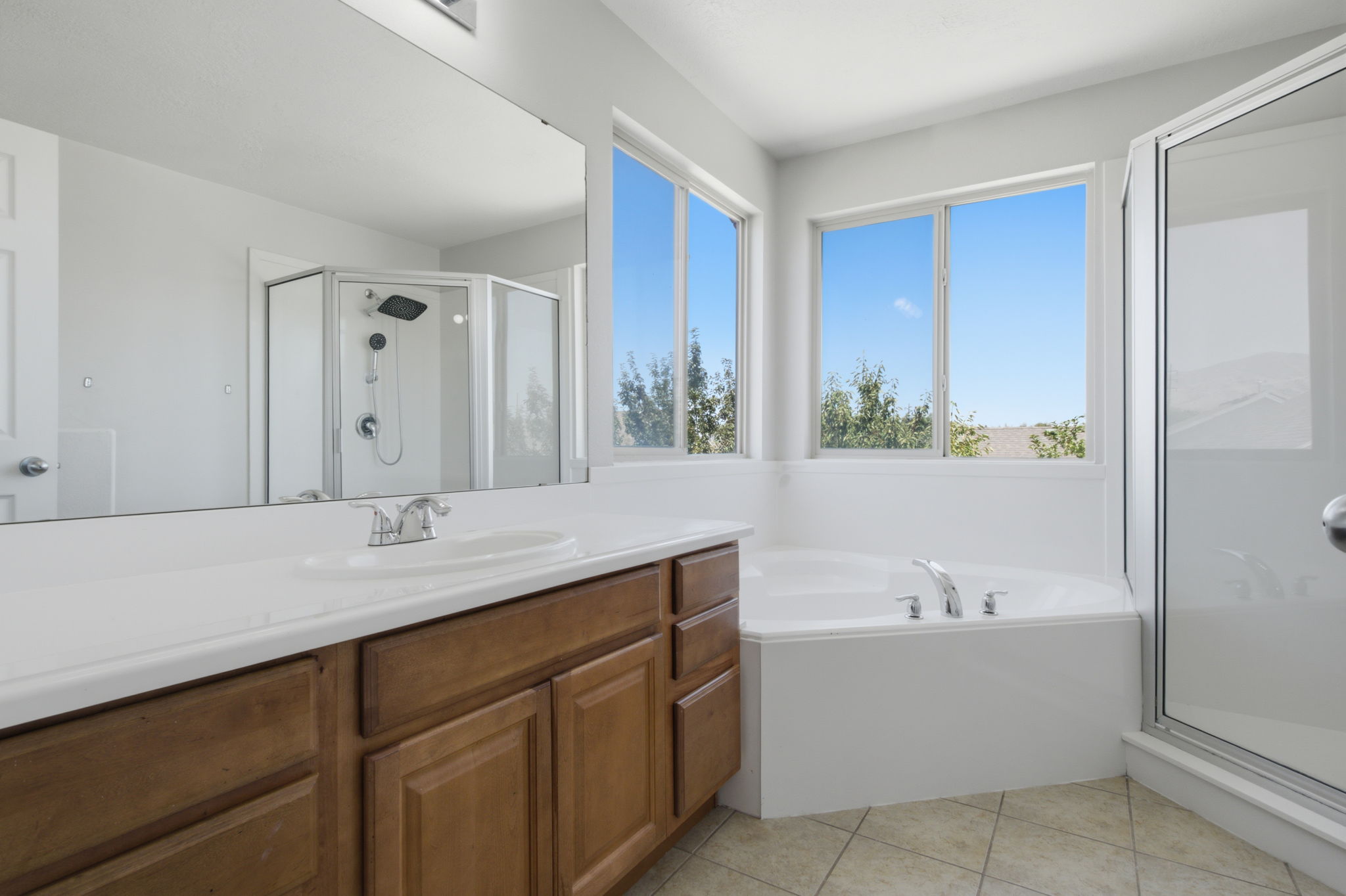 Spacious bathroom featuring a built-in soaking tub, separate shower enclosure with glass surround, and a vanity with a white countertop and wood-finish cabinetry