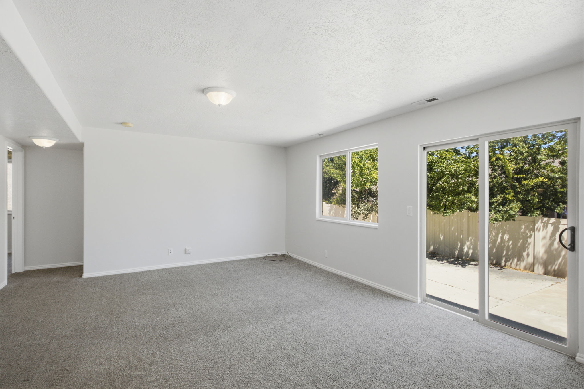 Spacious room featuring neutral carpeting, a large window, and a glass sliding door