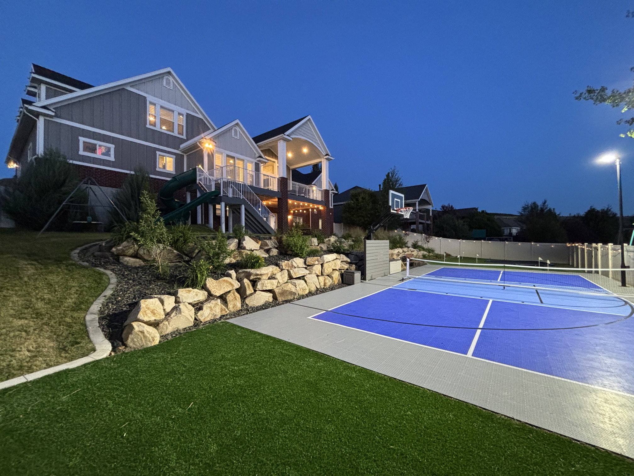 Multi-sport court featuring blue and grey surfacing, equipped with a basketball hoop and net