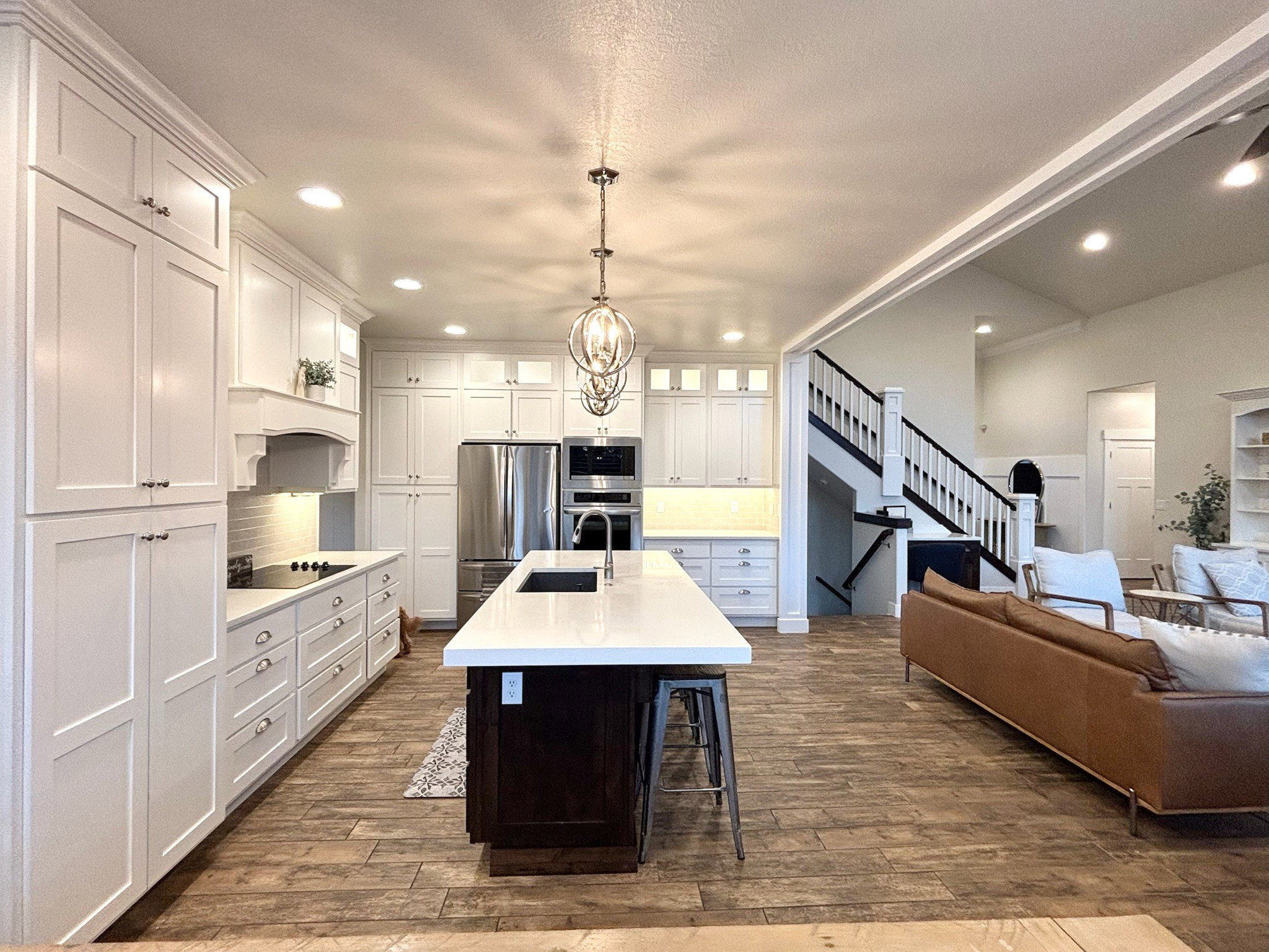 Open-concept kitchen featuring white shaker cabinetry, stainless steel appliances, a large center island with a sink, quartz countertops, and tile flooring.