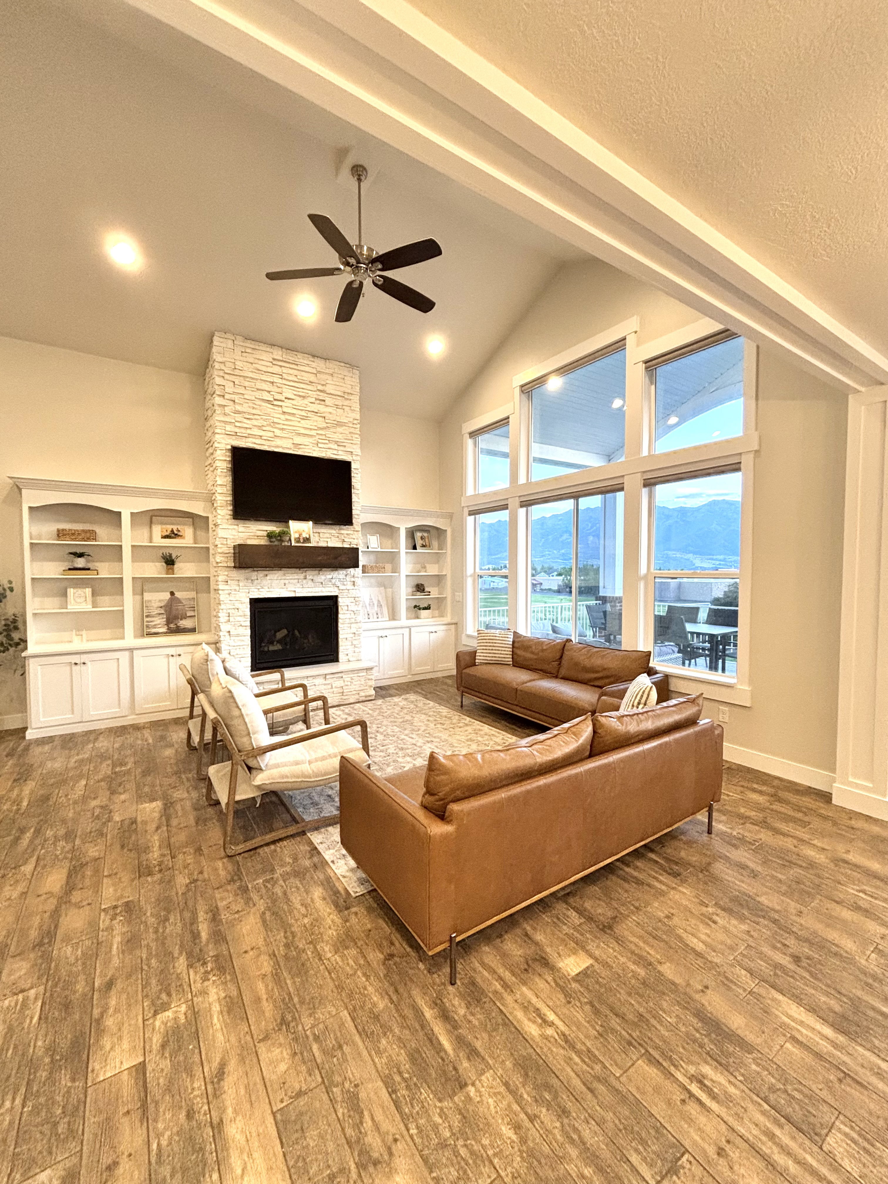 Spacious living area featuring vaulted ceilings, a stacked stone fireplace with wood mantel, built-in cabinetry, Tile flooring, and expansive windows