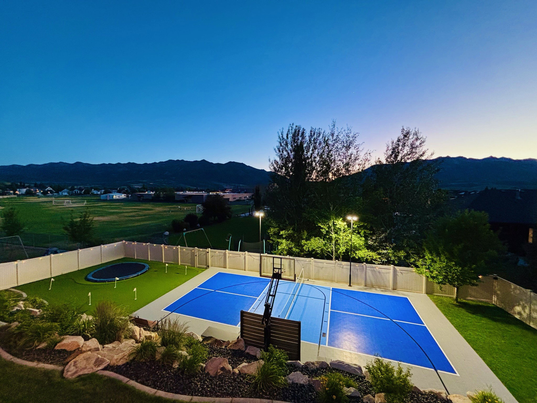 Backyard sports court featuring a blue playing surface and integrated basketball hoop