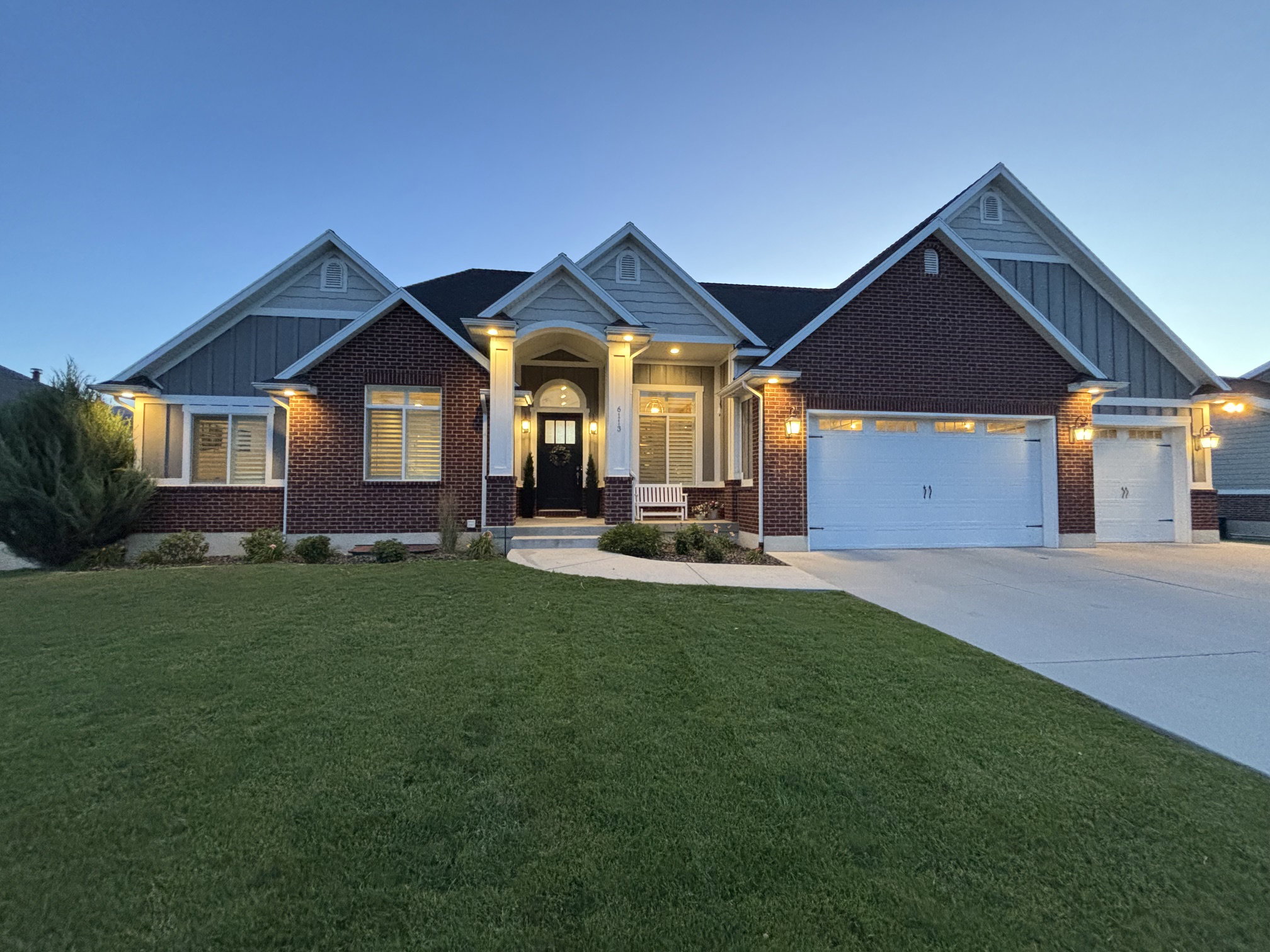Brick and siding exterior featuring gabled rooflines, a covered front entry with columns, a manicured lawn, and an attached two-car garage with a single-car garage