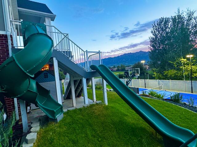 Exterior deck with white railings and dual green slides descending to a manicured lawn
