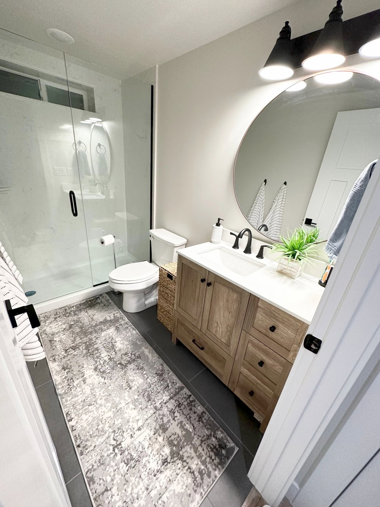 Modern bathroom featuring a wood-finish vanity with ample storage, a white countertop, and a circular mirror