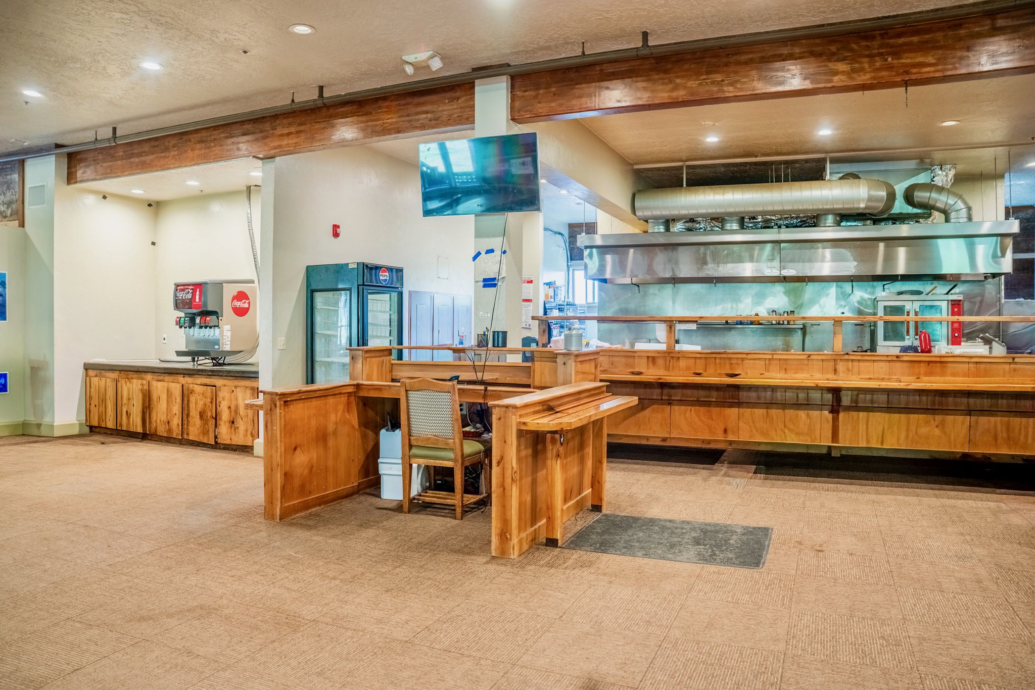 Commercial kitchen area featuring extensive wood cabinetry, stainless steel ventilation hood system, integrated beverage dispenser, and display refrigeration