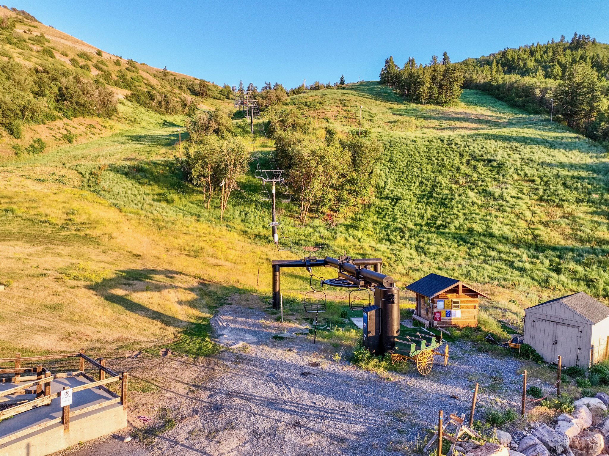 Expansive mountain property featuring a ski lift structure, a small wood-sided cabin with a dark roof, a light-colored shed, and an open gravel area