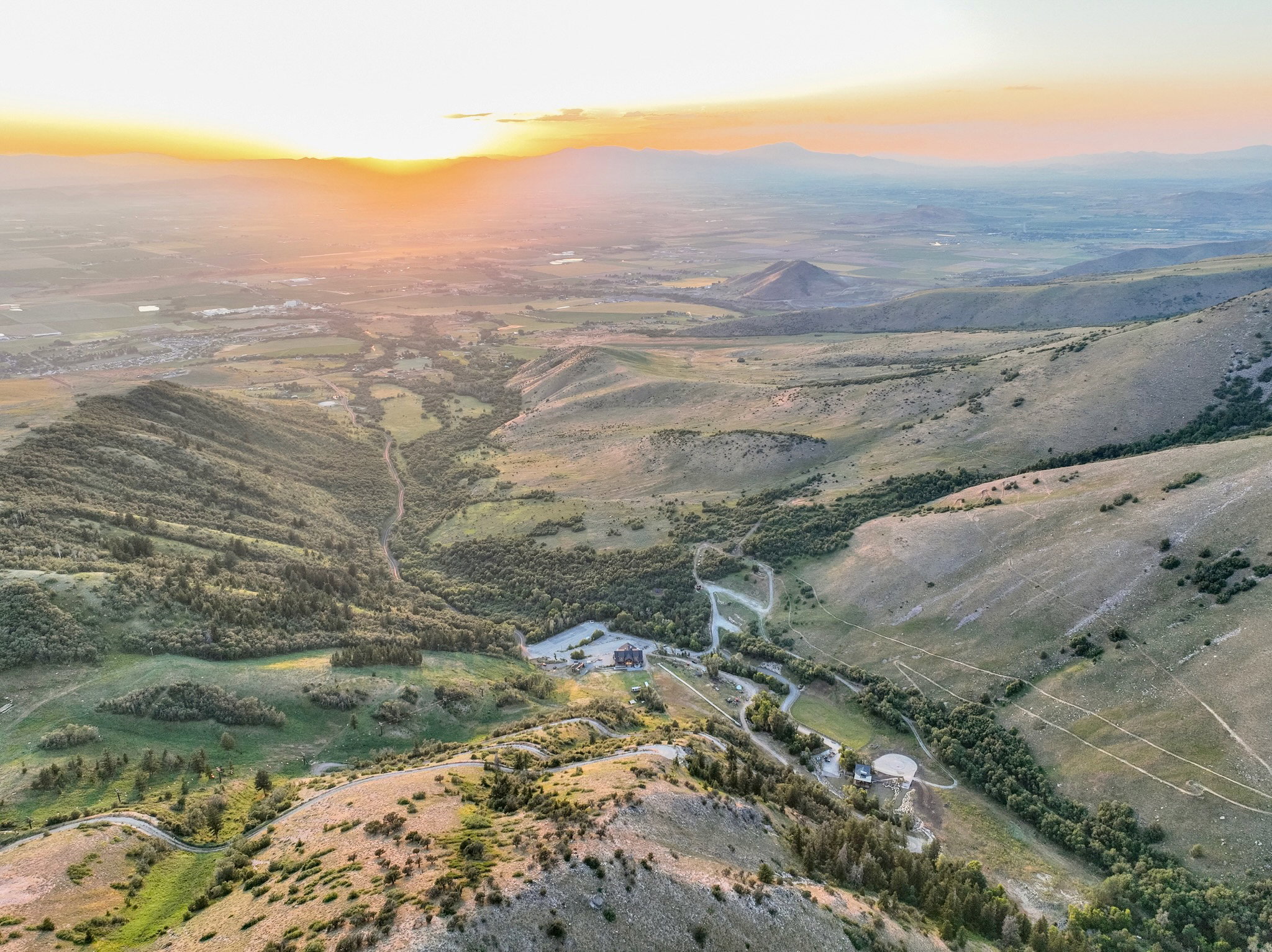 Sprawling landscape featuring expansive mountain ranges, green valleys, and distant structures under a vibrant sky