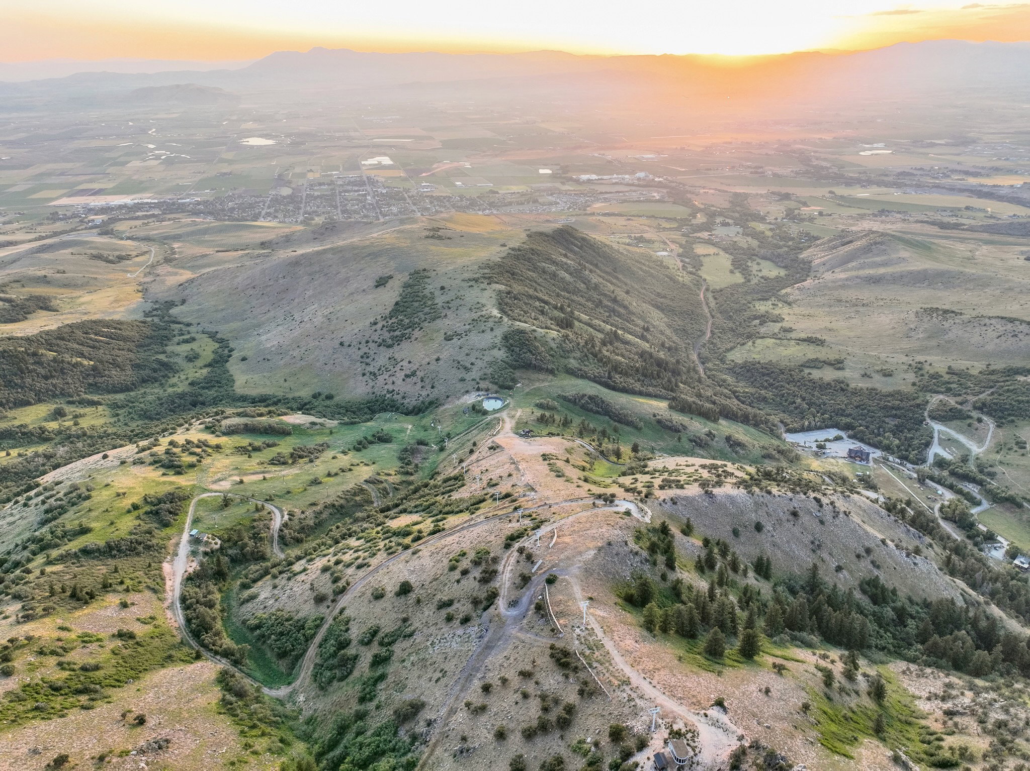 Expansive mountain landscape featuring varied terrain, scattered trees, and distant urban development