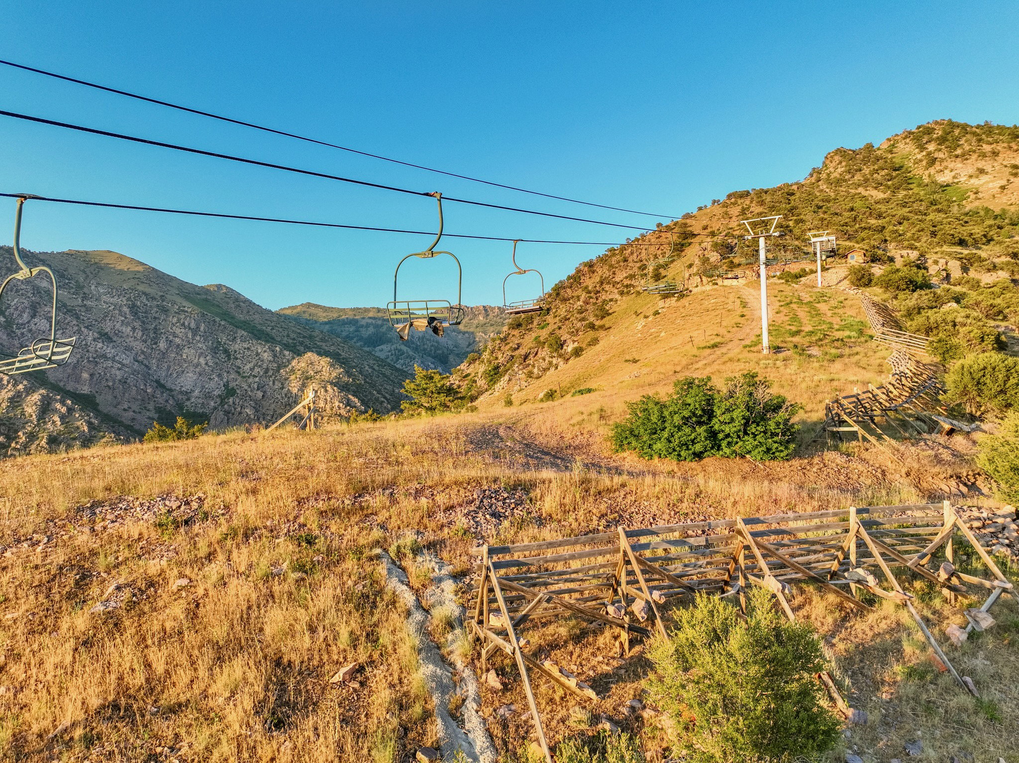 Mountainous terrain featuring a chairlift system, dry grasses, and scattered green foliage