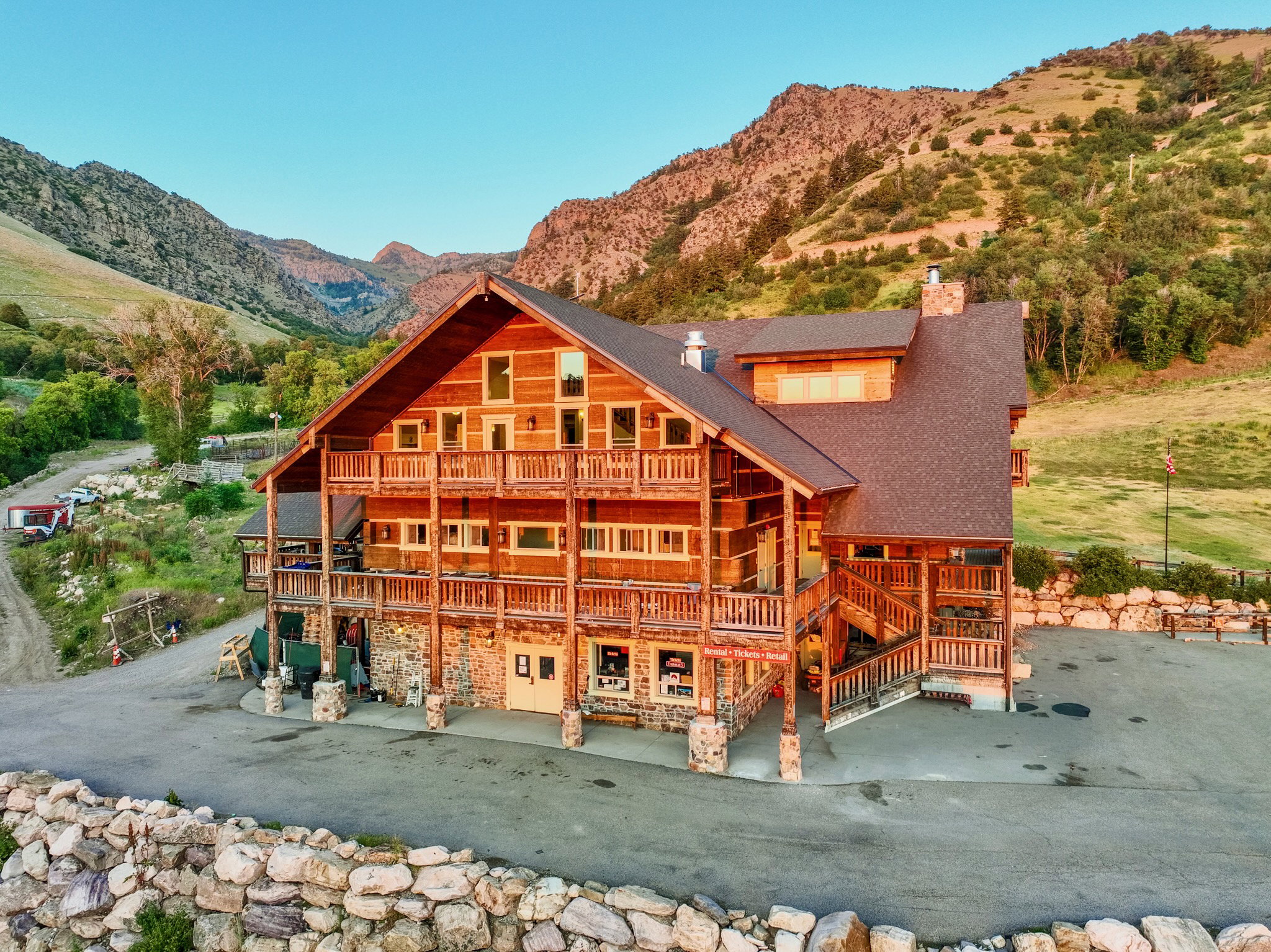 Expansive log and stone construction with multi-level balconies, a tiered wood-shingle roof, and a large paved parking area