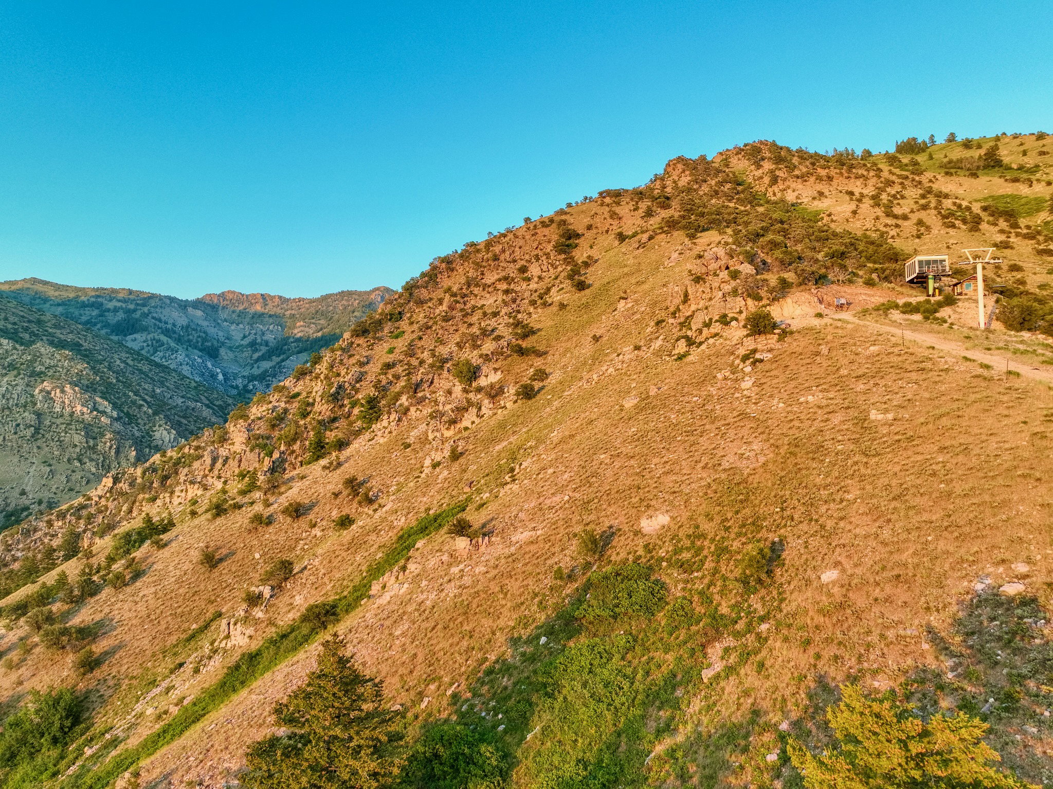 Mountainous terrain featuring a ski lift structure, a dirt path, and scattered evergreen trees