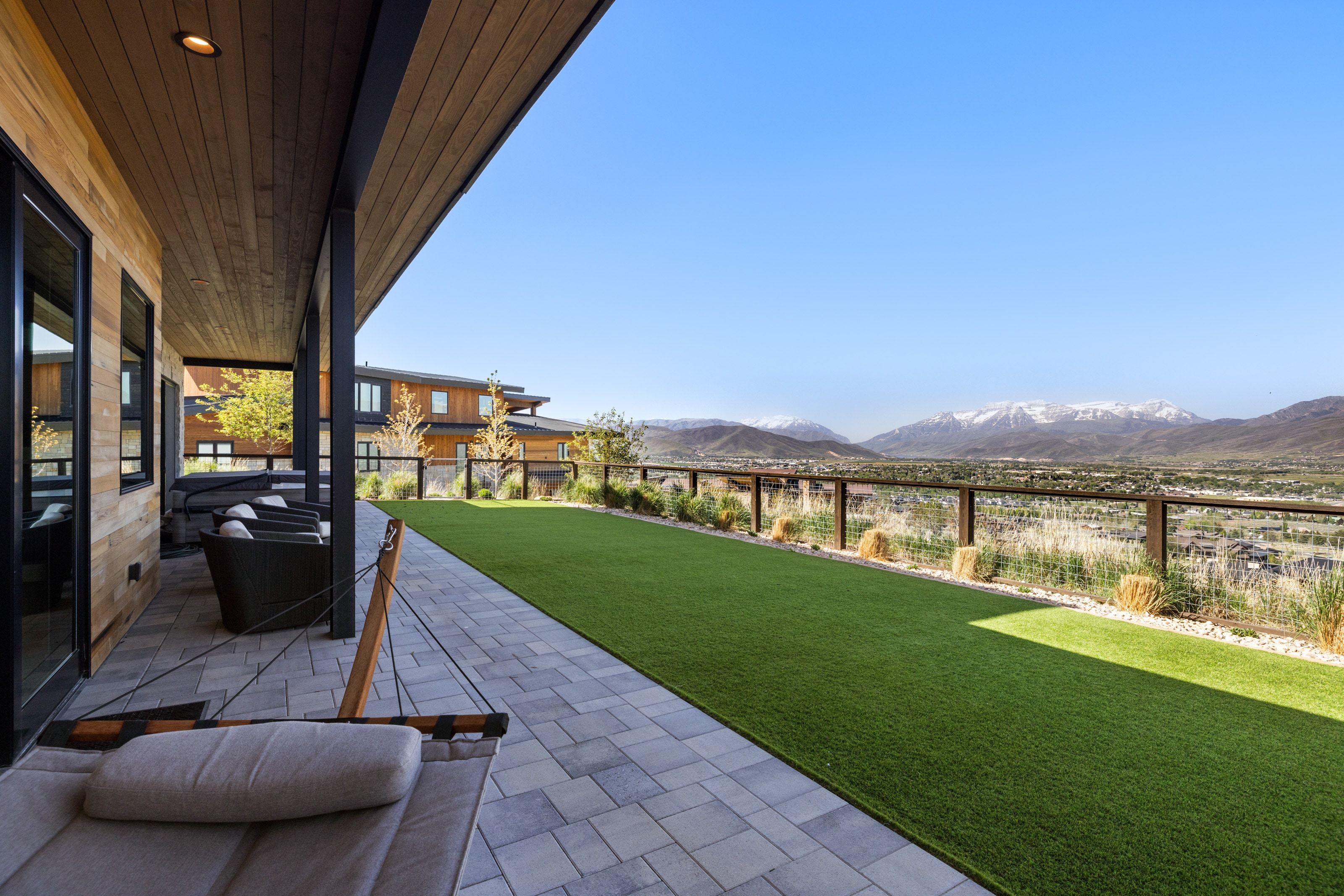 Expansive outdoor patio featuring paver flooring, an artificial turf lawn, and a clear safety railing